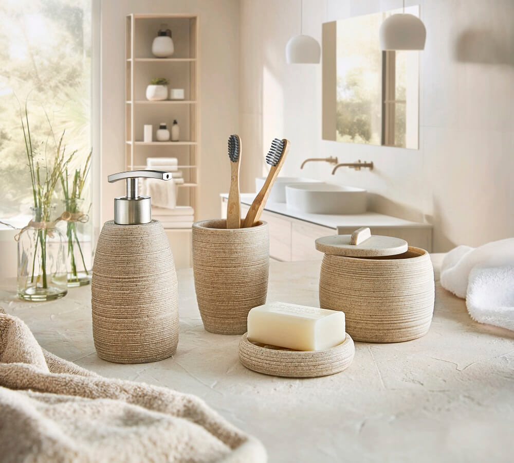 Beiges Badezimmer-Set mit Seifenspender, Zahnputzbecher und Aufbewahrungsbehältern auf einer Steinarbeitsplatte. Sanfte Beleuchtung und moderne Dekoration im Hintergrund.