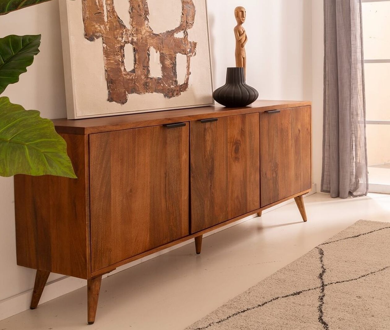 Langes Sideboard aus warmem Akazienholz mit drei Türen und schrägen Beinen im Mid-Century-Stil, dekoriert mit Skulptur und Vase.