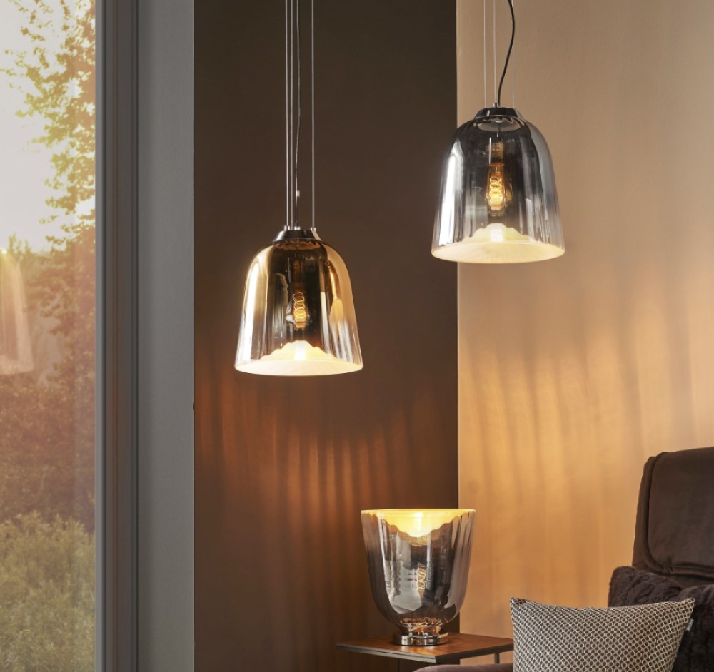Zwei moderne Pendelleuchten und eine Tischleuchte mit Metallic-Schirmen erhellen eine gemütliche Wohnzimmerecke in der Nähe eines großen Fensters.