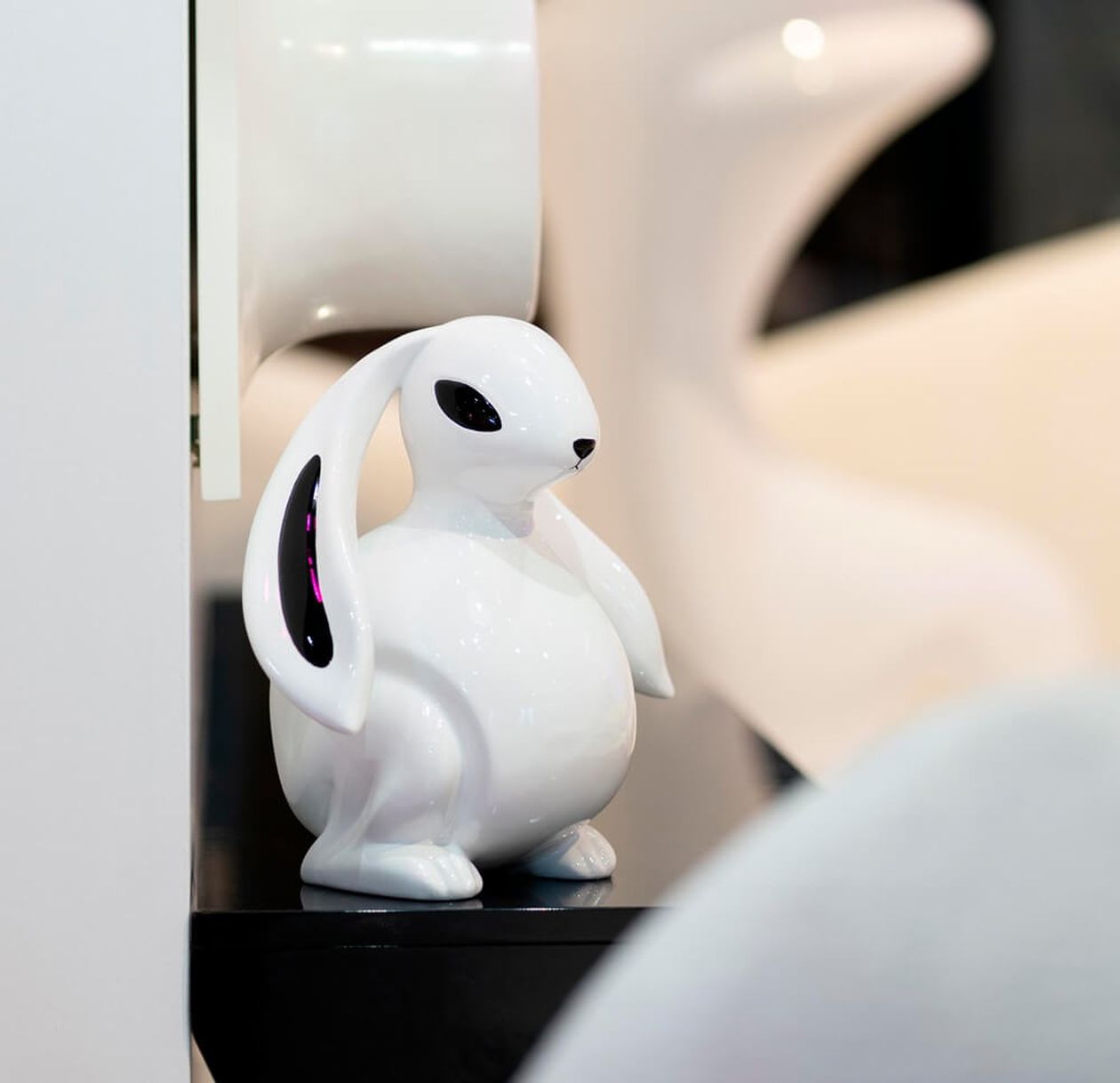 Weiße Dekofigur in Form eines Hasen mit langen Ohren und schwarzen Akzenten sitzt auf einer schwarzen Fläche, moderner, verspielter Einrichtungsstil.
