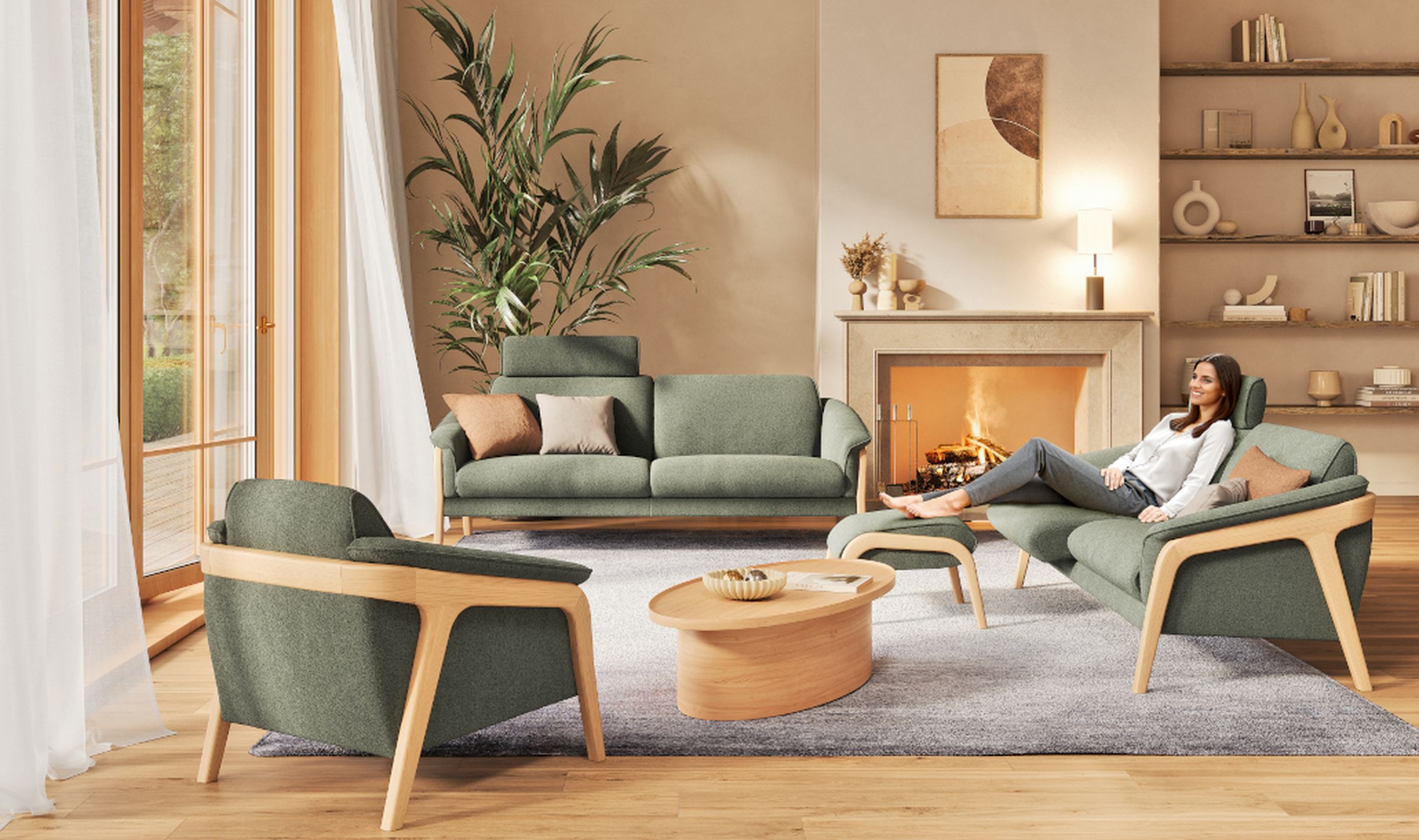 Eine Sitzgruppe aus Polstermöbeln der Transforma-Serie Nido der SEGMÜLLER Werkstätten mit hellen Holzgestellen und grünen Stoffbezügen steht in einem modernen Wohnzimmer mit Kamin. Eine Frau sitzt gemütlich auf einem Zweisitzer mit ergonomischen Hocker.