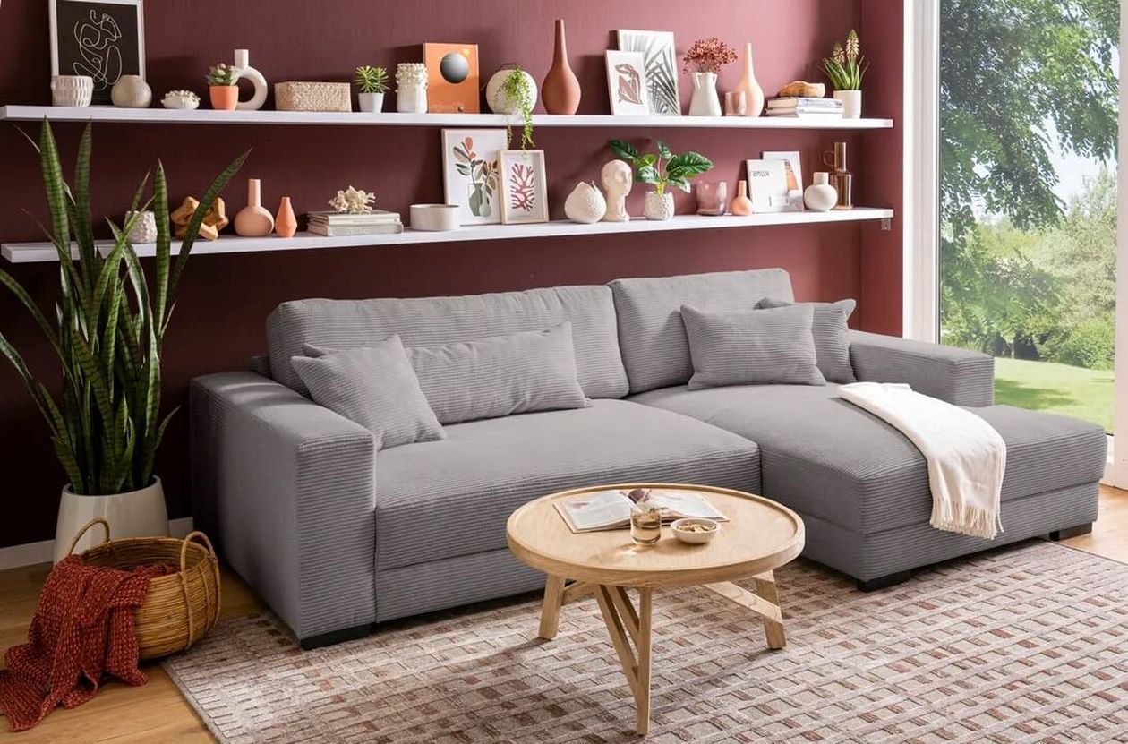 Modernes Wohnzimmer mit einem grauen Sofa, einem Couchtisch aus Holz, dekorativen Regalen und einem großen Fenster mit Blick ins Grüne.