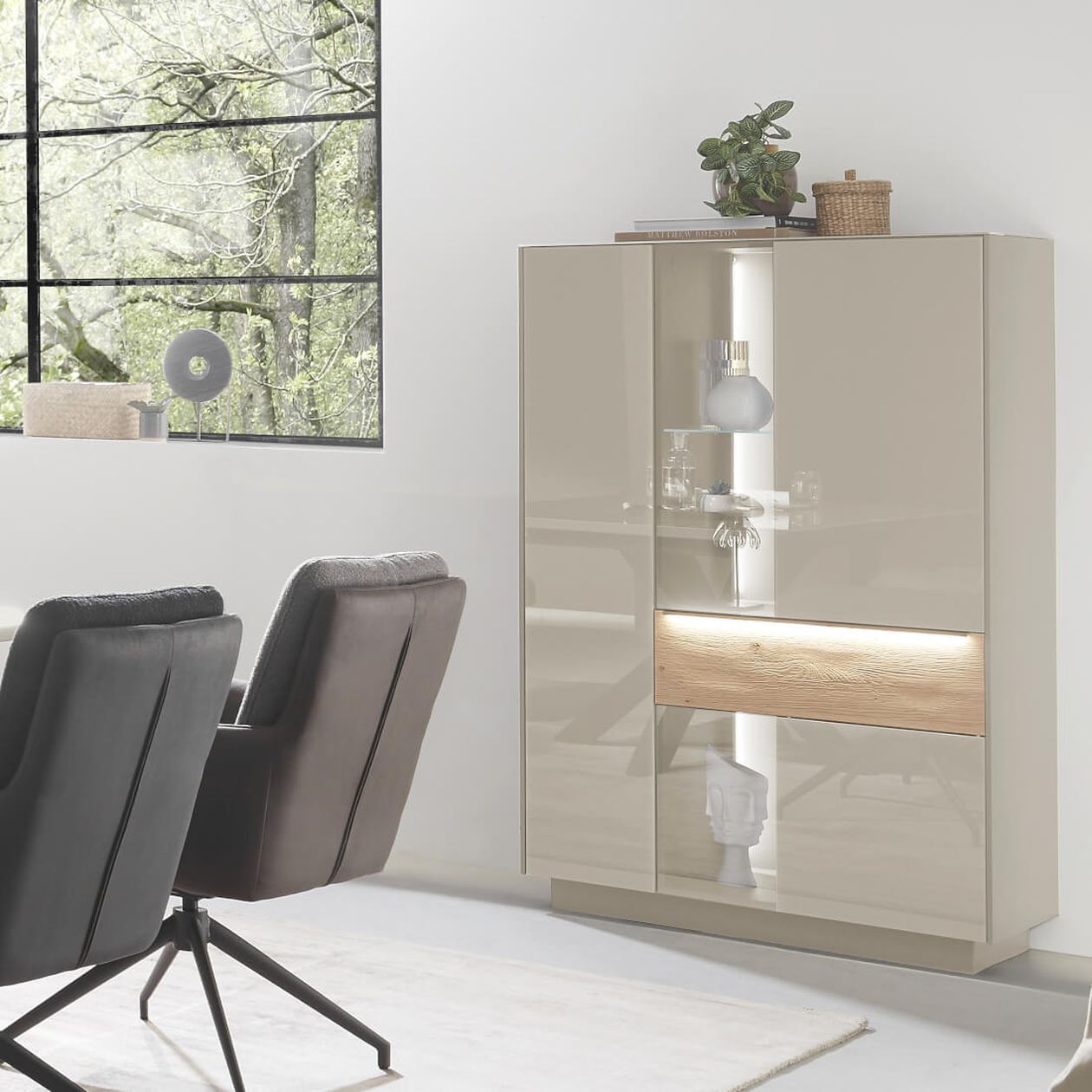 Kommode mit Glastüre, auf der eine Pflanze und ein Aufbewahrungskorb steht. Daneben zwei Stühle aus Leder.