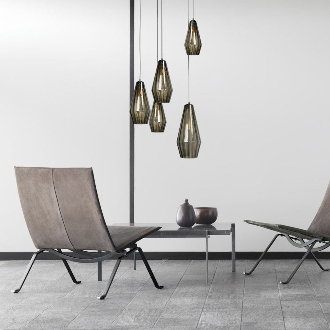 Charaktervolle Pendelleuchte mit strukturierten, dunkelgrün getönten Glasschirmen setzt stilvolle Highlights über zwei Ledersesseln auf grauen Steinfliesen. Perfekt für ein hochwertiges, designorientiertes Ambiente.