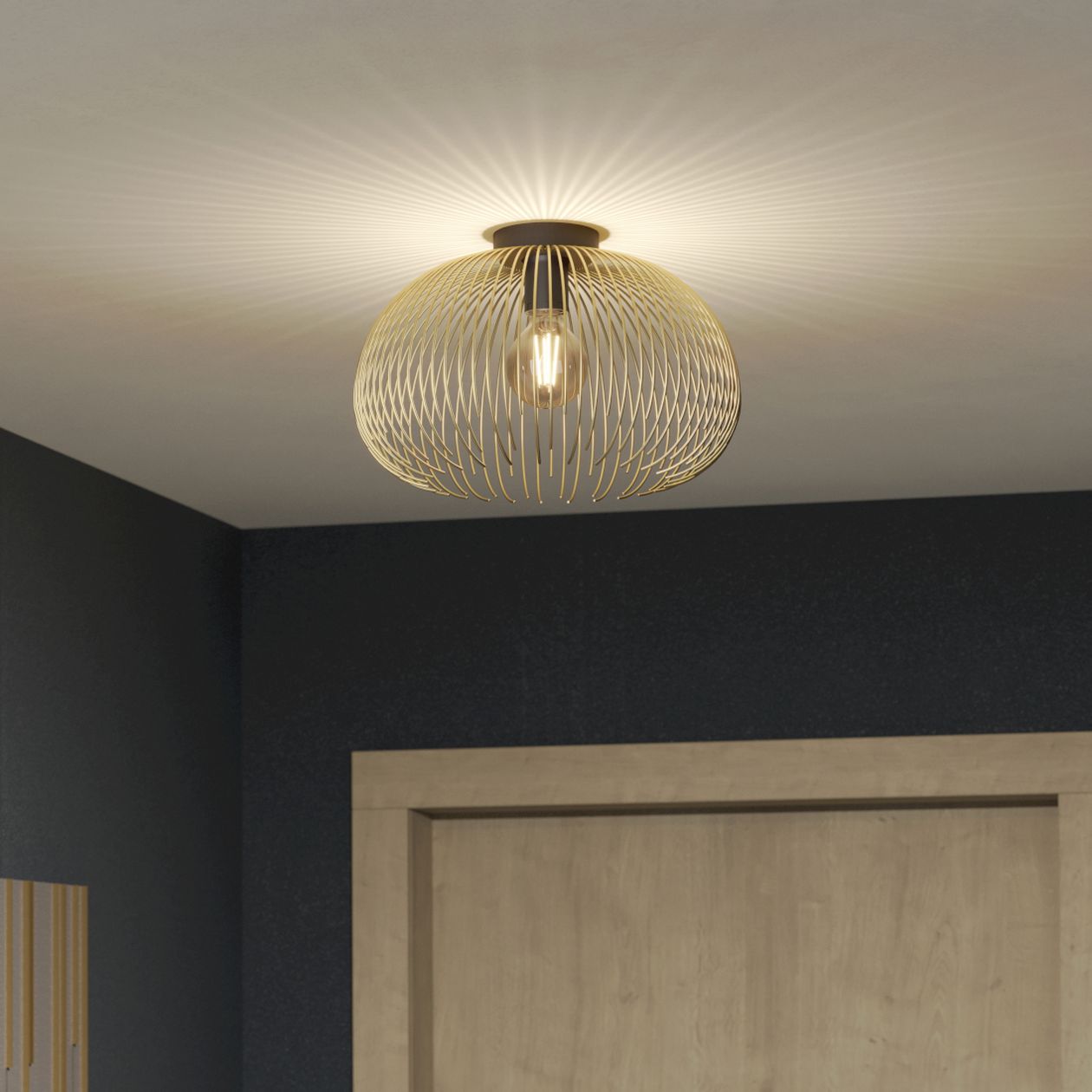 Goldfarbene kugelförmige Deckenleuchte mit Drahtgeflechtdesign, die sanfte Lichtmuster an die Decke wirft. Dunkle Wände und ein Türrahmen aus Holz.
