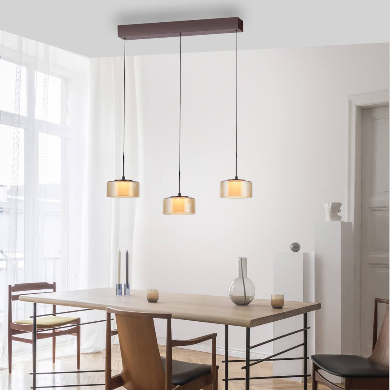 Schlanke Pendelleuchte mit drei leicht getönten Glasschirmen verleiht dem Holzesstisch eine dezente, moderne Eleganz. Ideal für natürliche und zeitgemäße Wohnräume.