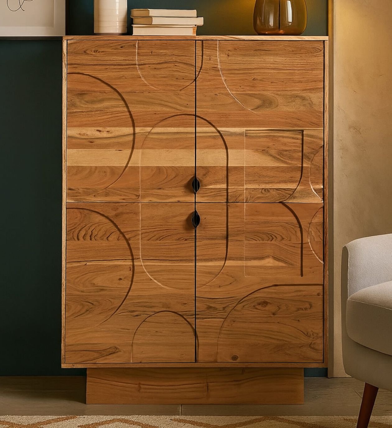 Holzschrank mit kreisförmigen Mustern auf den Türen, zwei schwarzen Griffen und Büchern darauf, neben einem gerahmten Wandfoto und einem weißen Stuhl.