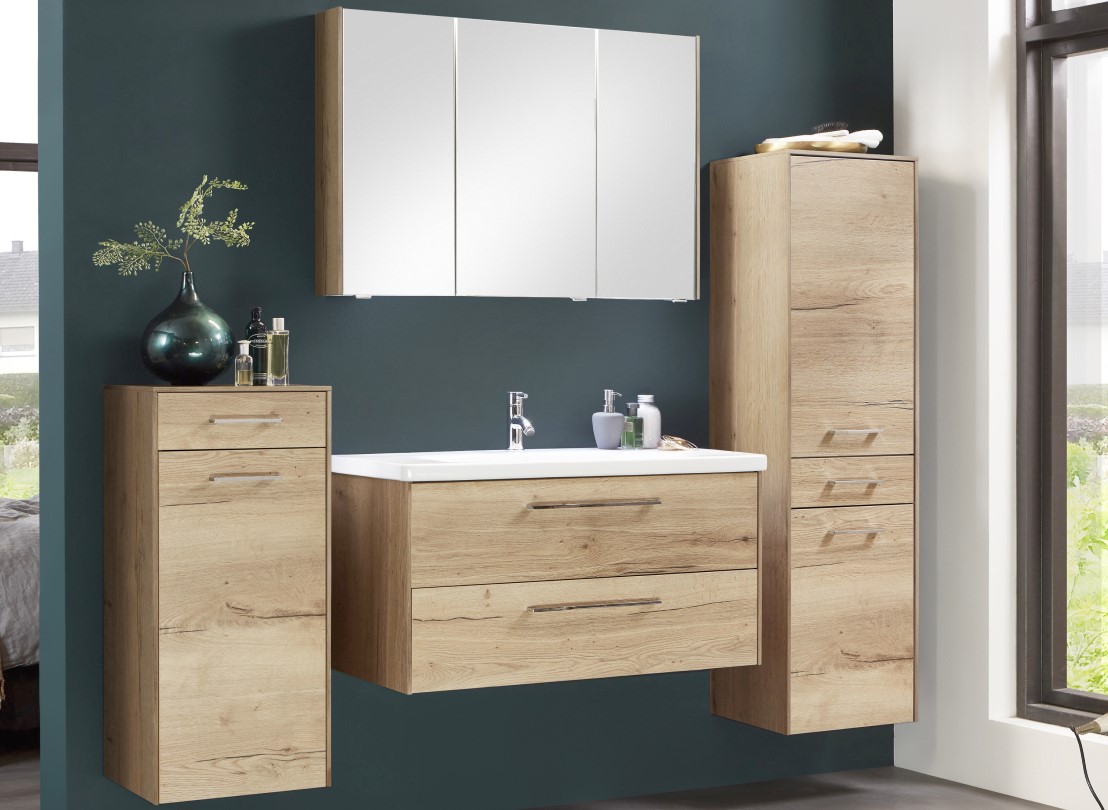 Modernes Badezimmer mit Schränken in Holzoptik, einem weißen Waschbecken, einem großen Spiegel und dekorativen Pflanzen vor einer dunkelgrünen Wand.