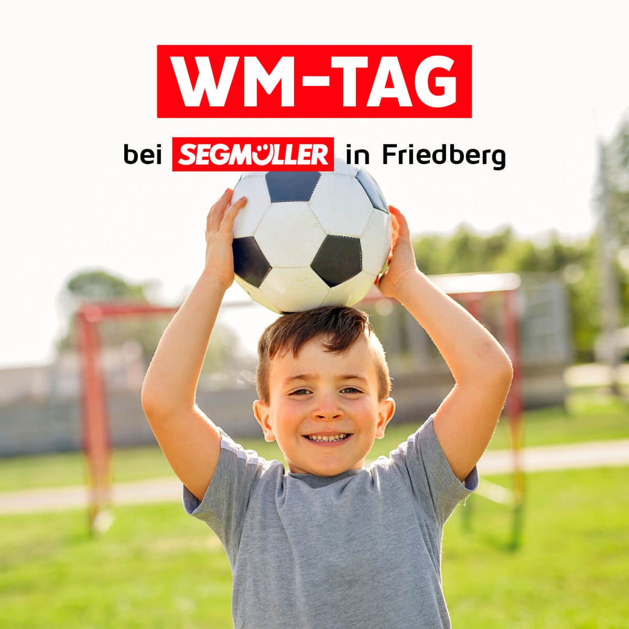 Junge hält Fußball über dem Kopf, lächelt auf einem Spielfeld. Text: "WM-TAG bei Segmüller in Friedberg".