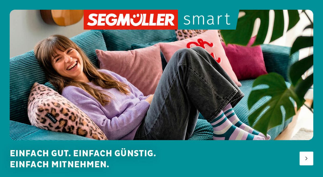In einer Werbung für SEGMÜLLER Smart entspannt eine lächelnde Person auf einem türkisfarbenen Sofa mit bunten Kissen.