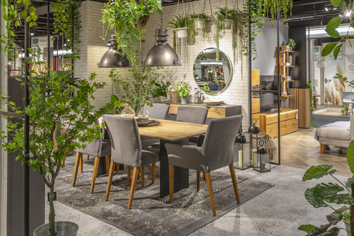 Graue Stühle mit Holzbeinen der MAISON-Serie Nashville stehen in einem mit Pflanzen dekoriertem Ausstellungsraum für Speisezimmermöbel.