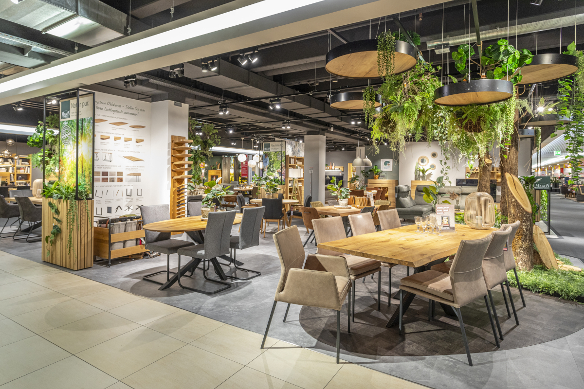 MAISON Möbel stehen in einem Ausstellungsraum für Speisezimmermöbel. Darunter sind Stühle der Serie Memphis mit beigen Lederbezügen und der Esstisch Fresno mit Holzplatte und einem Gestell aus pulverbeschichtetem Metall.