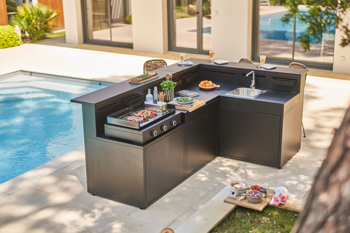 Neben einem Pool steht eine Outdoorküche mit dem schwarzen Plancha Modern Gas Plancha 75 der marke Forge Adour.