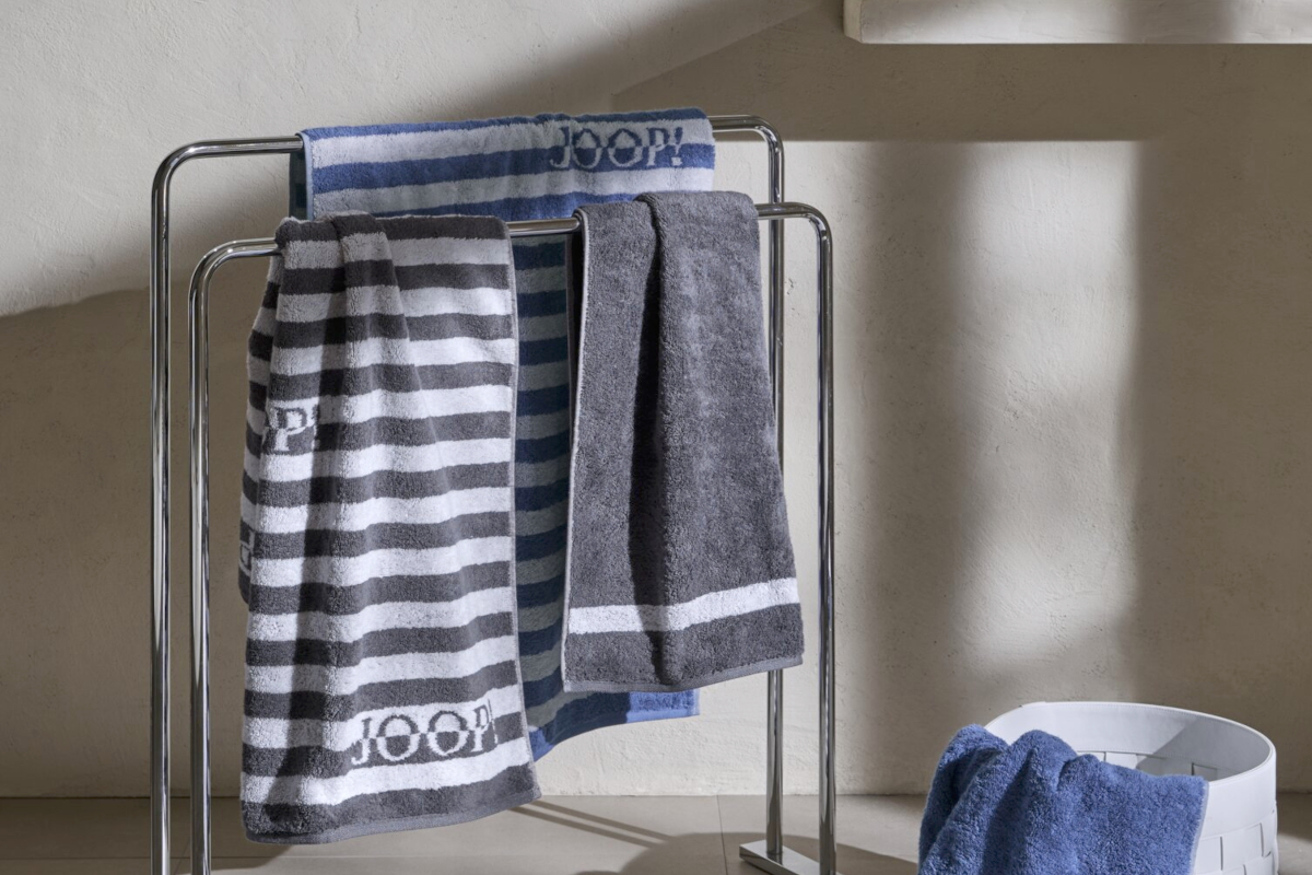 Mediterranes Badezimmer mit Handtuchhalter und darauf dem Handtuch Split Stripes von JOOP! mit blauen und weißen Streifen und dem Logo der Marke