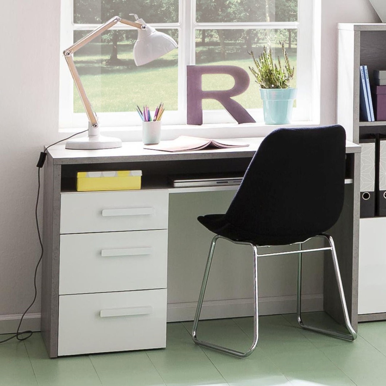 Auf dem Foto befindet sich ein grauer Kunststoff-Jugendschreibtisch mit weißen Schubladen. Davor steht ein schwarzer Stuhl mit Metallbeinen.