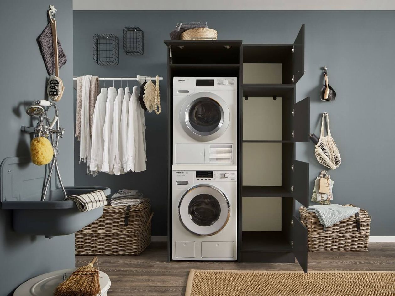 Waschküche mit Waschmaschine und Trockner, offenem Schrank und hängender Kleidung.