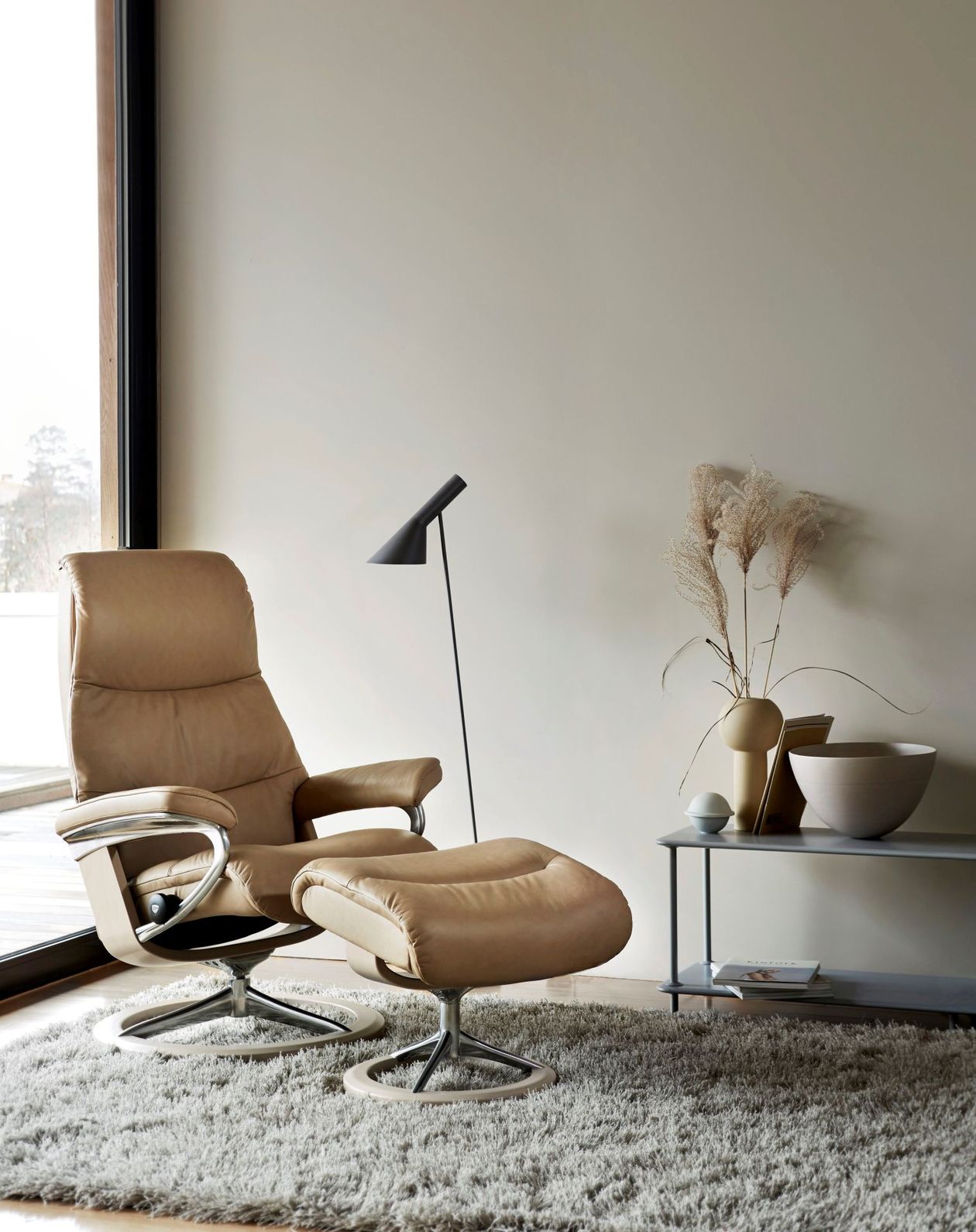 Ein Relaxsessel aus Leder in Beige mit passendem Fußhocker in einem minimalistisch eingerichteten Raum.