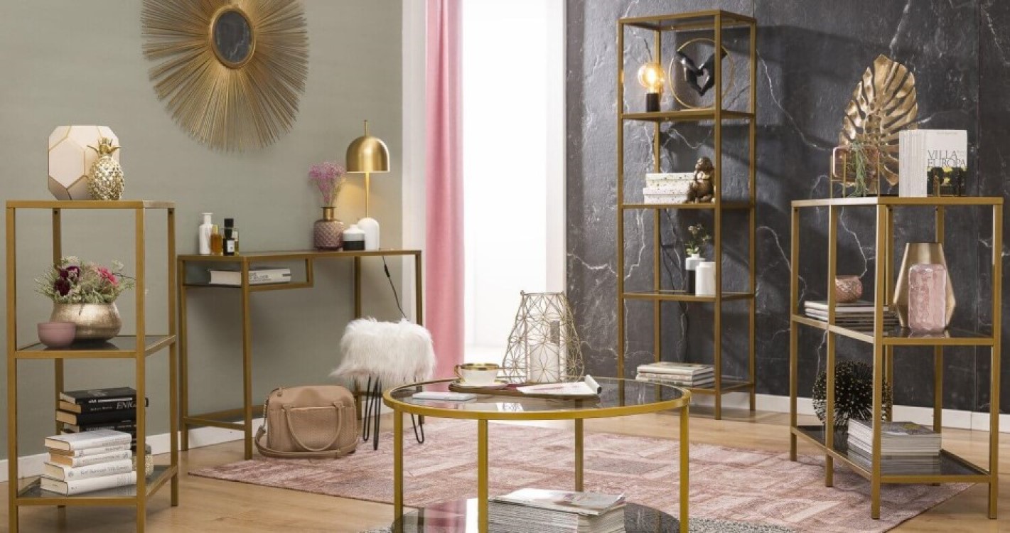 Moderne Wohnzimmereinrichtung mit gold-akzentuierten Möbeln, dekorativen Regalen, einem runden Glastisch und einem Sonnen-Spiegel an der Wand.