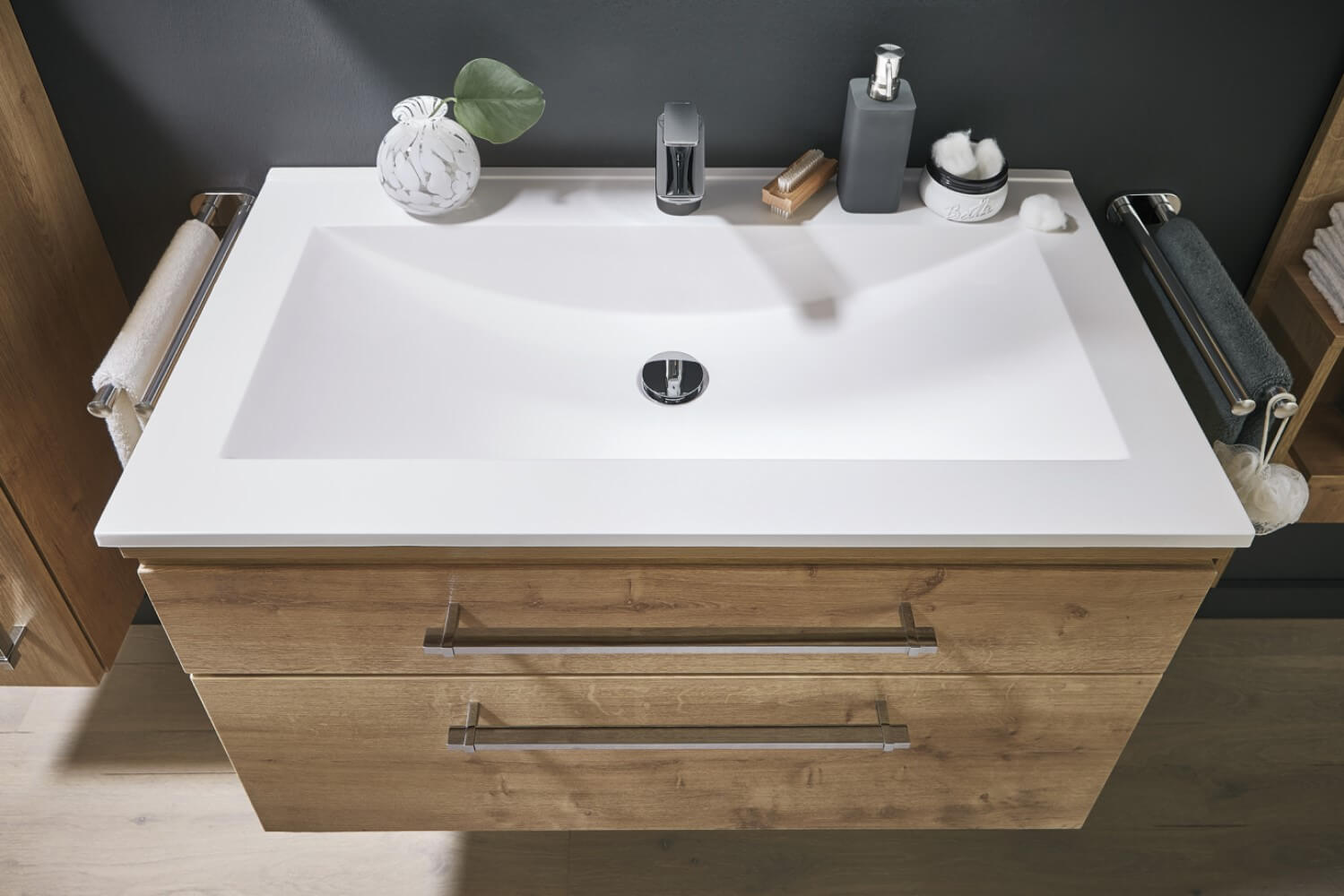 Modernes Badezimmerwaschbecken mit einem weißen Becken, einem Holzschrank und silbernen Griffen.