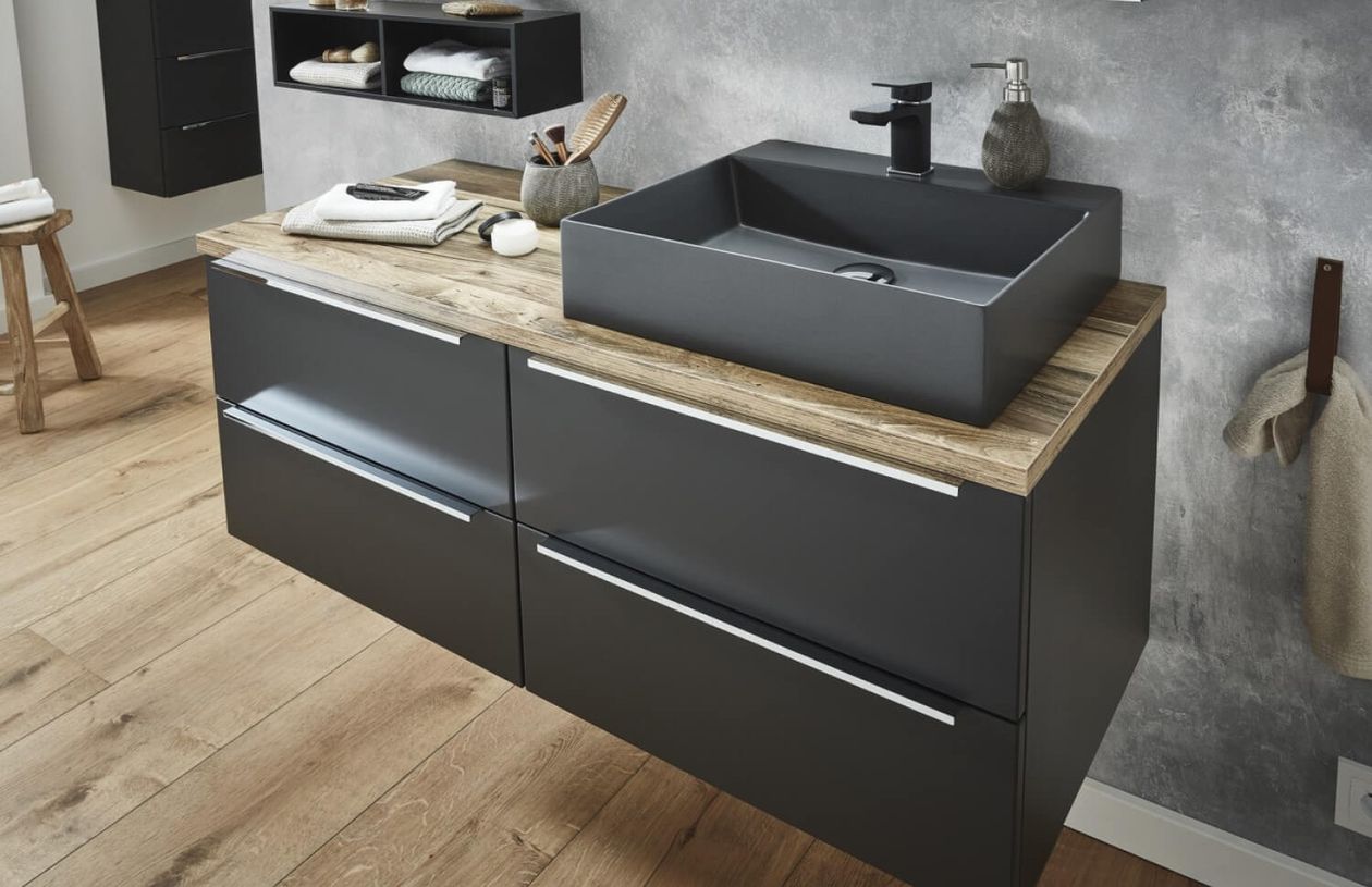 Modernes Badezimmer mit einem schwarzen rechteckigen Waschbecken auf einer Holzarbeitsplatte, dunklen Schränken und einer grauen strukturierten Wand.