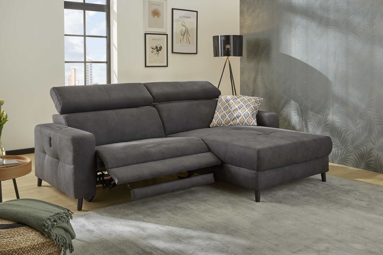 Moderne Wohnzimmereinrichtung mit einem dunkelgrauen Ecksofa, dekorativen Kissen, einer Stehlampe, gerahmter Kunst an der Wand und einem großen Fenster.