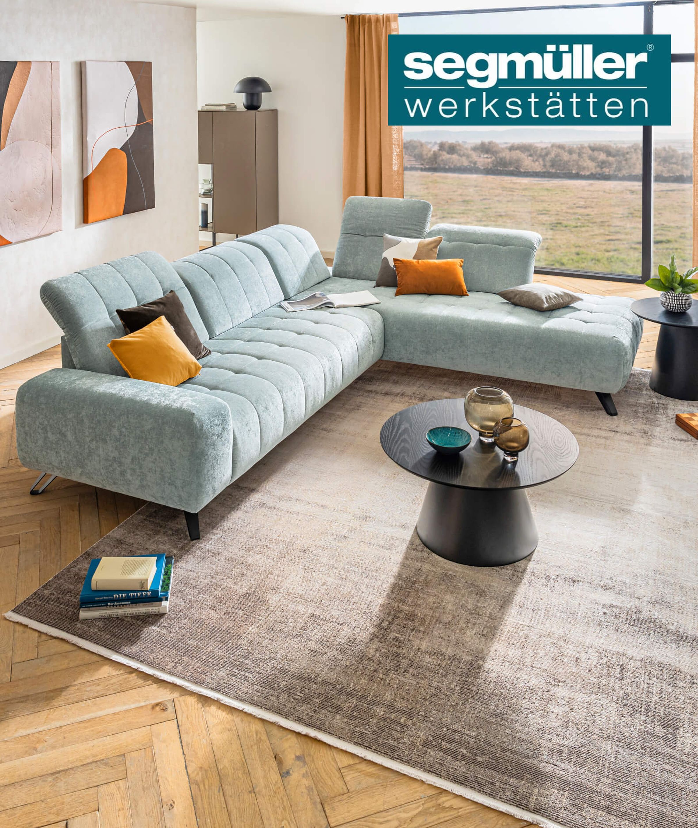 Helles Wohnzimmer mit einer großen, hellblauen Sofaecke, bunten Kissen, Holzboden, modernen Kunstwerken und einem runden Couchtisch.