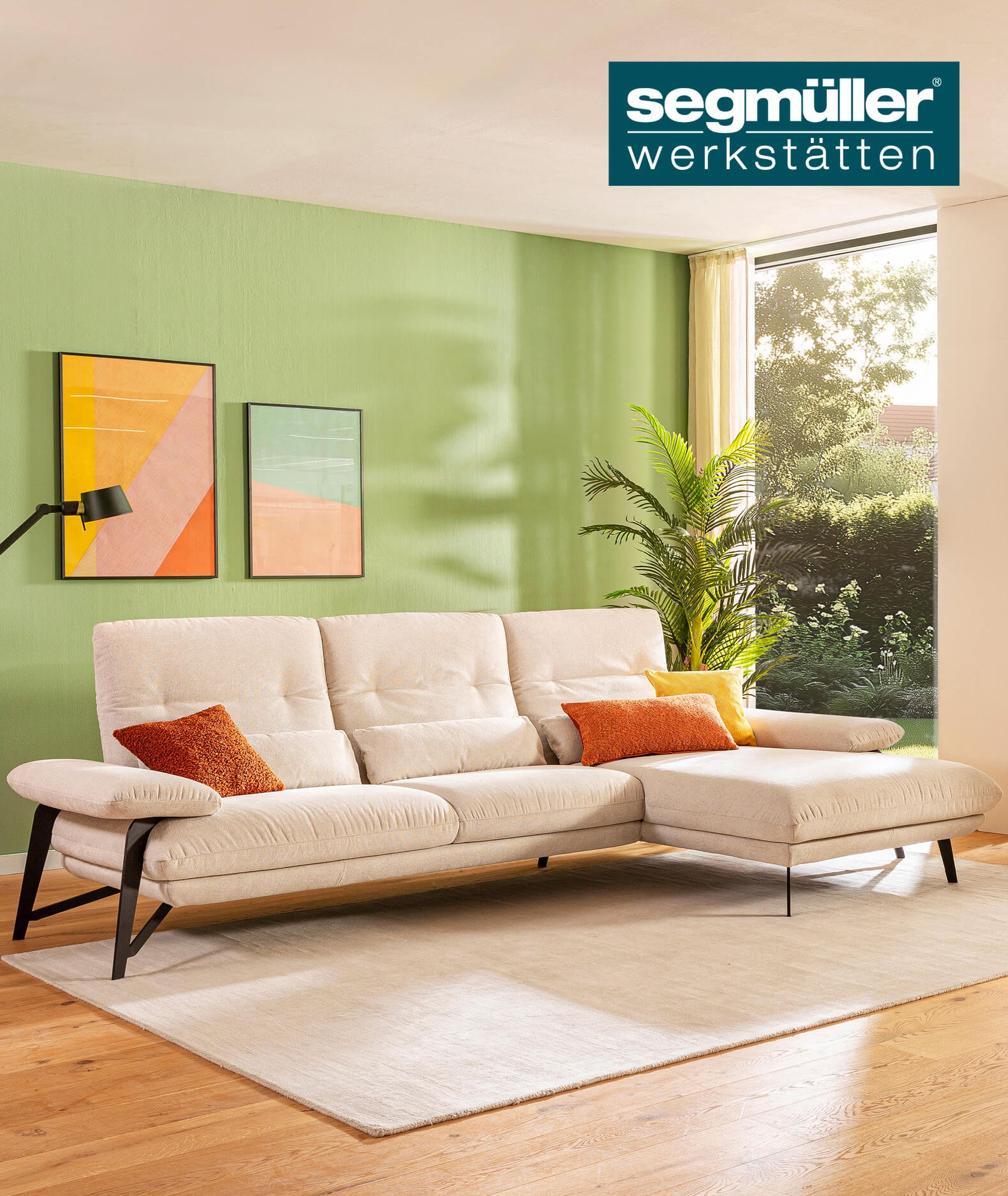 Ecksofa Denise aus den SEGMÜLLER WERKSTÄTTEN mit cremefarbenem Stoffbezug und schwarzen Füßen vor einer grünen Wand.