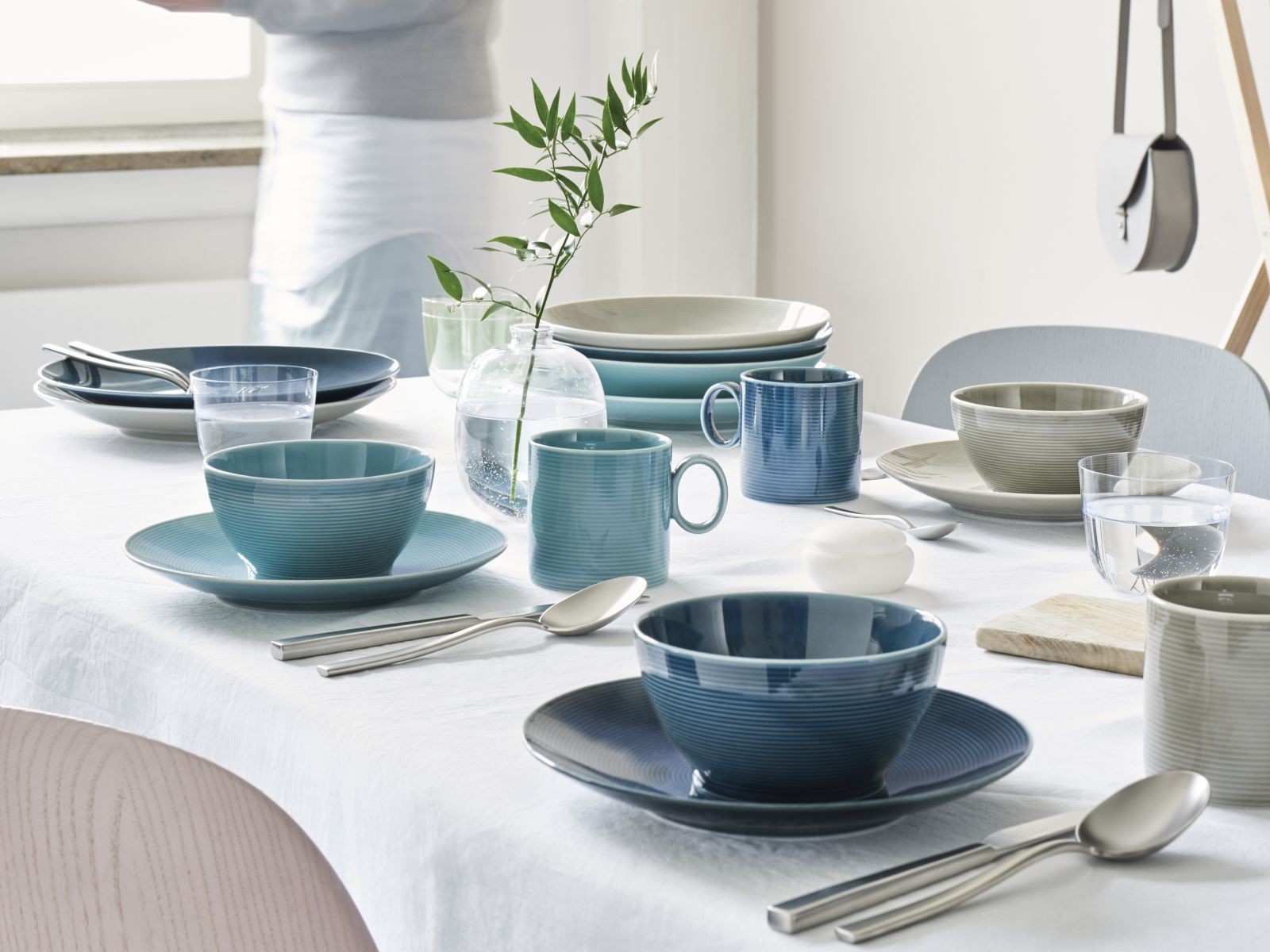 Ein Tisch mit weißer Tischdecke ist gedeckt mit dem Thomas-Kombiservice Loft, bestehend aus Tassen, Tellern und Schüsseln aus Porzellan in den Farben Blau, Hellblau und Weiß.
