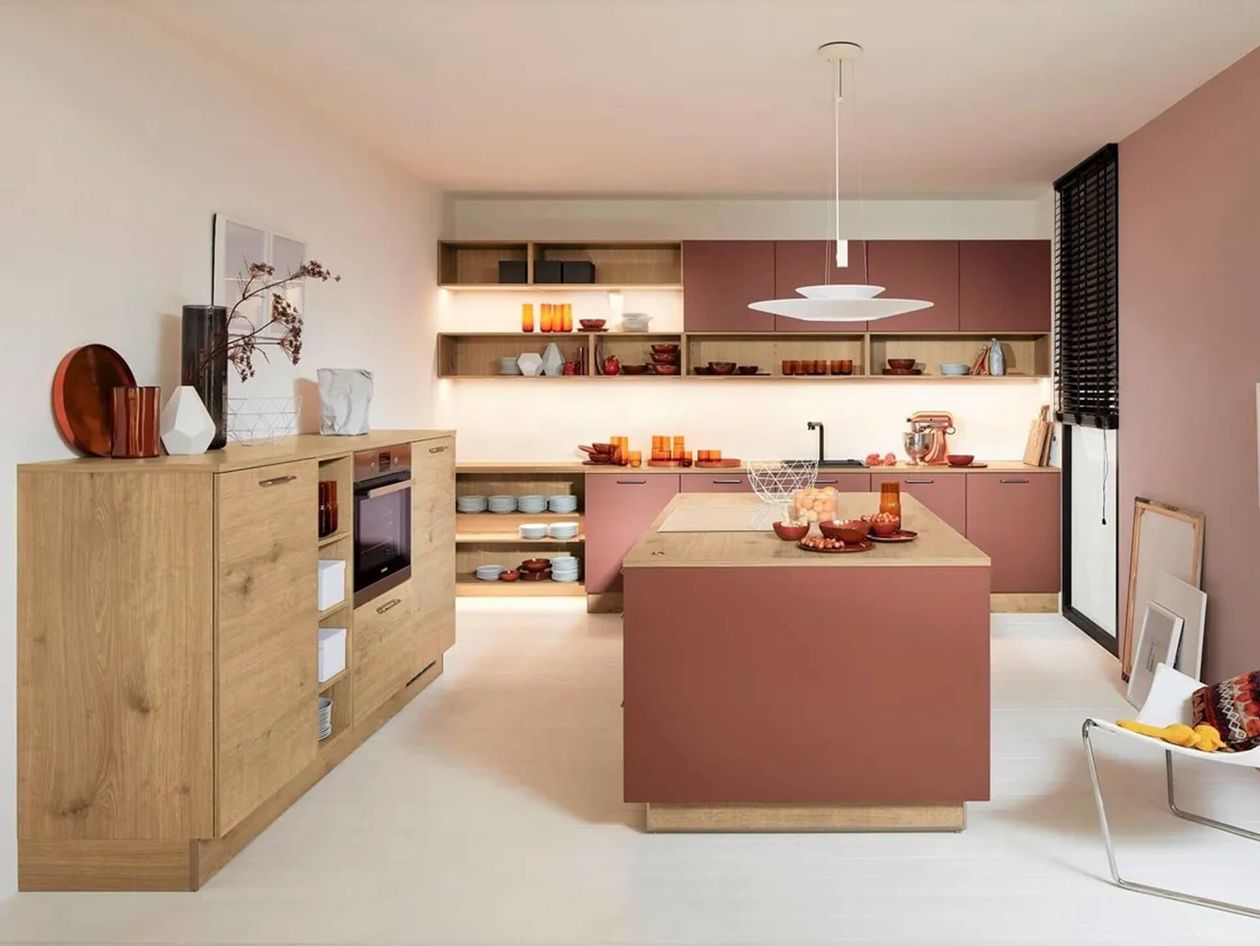 Halbblick auf eine ähnlich eingerichtete moderne Küche im sanften Rosa- und Holztönen, mit offenen Regalen, dekorativem Geschirr und gemütlicher Atmosphäre.