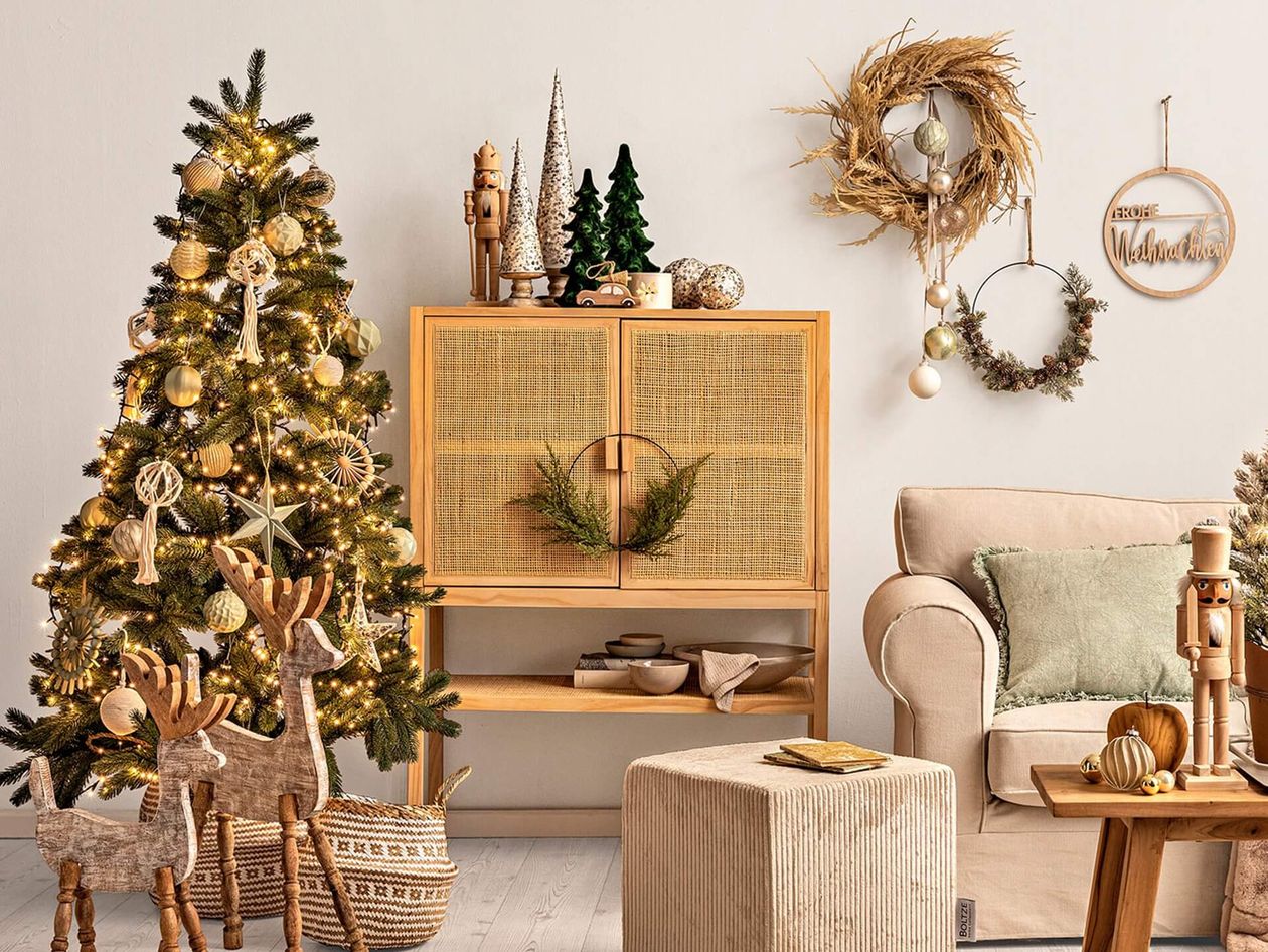 Gemütliches Wohnzimmer mit einem geschmückten Weihnachtsbaum, Weidenrentieren, einem beigen Sofa und festlichen Kränzen an der Wand.