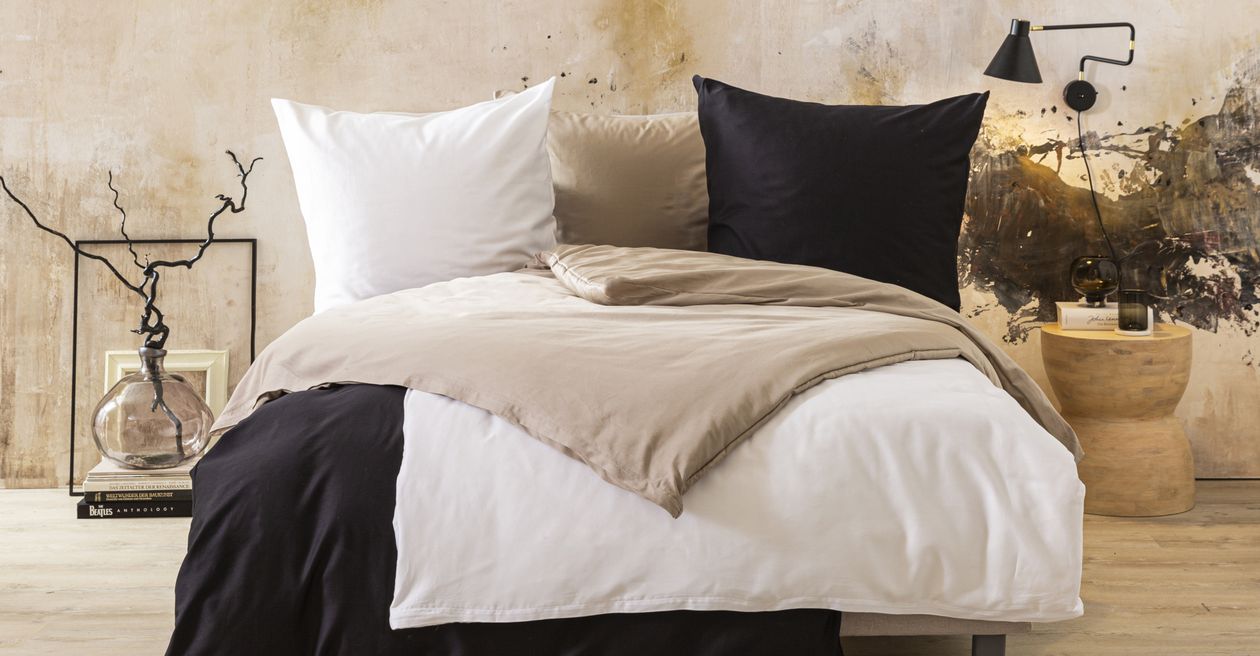 Die Satin-Bettwäsche Anna von Fürstenhof in Weiß, Creme und Anthrazit auf einem Bett