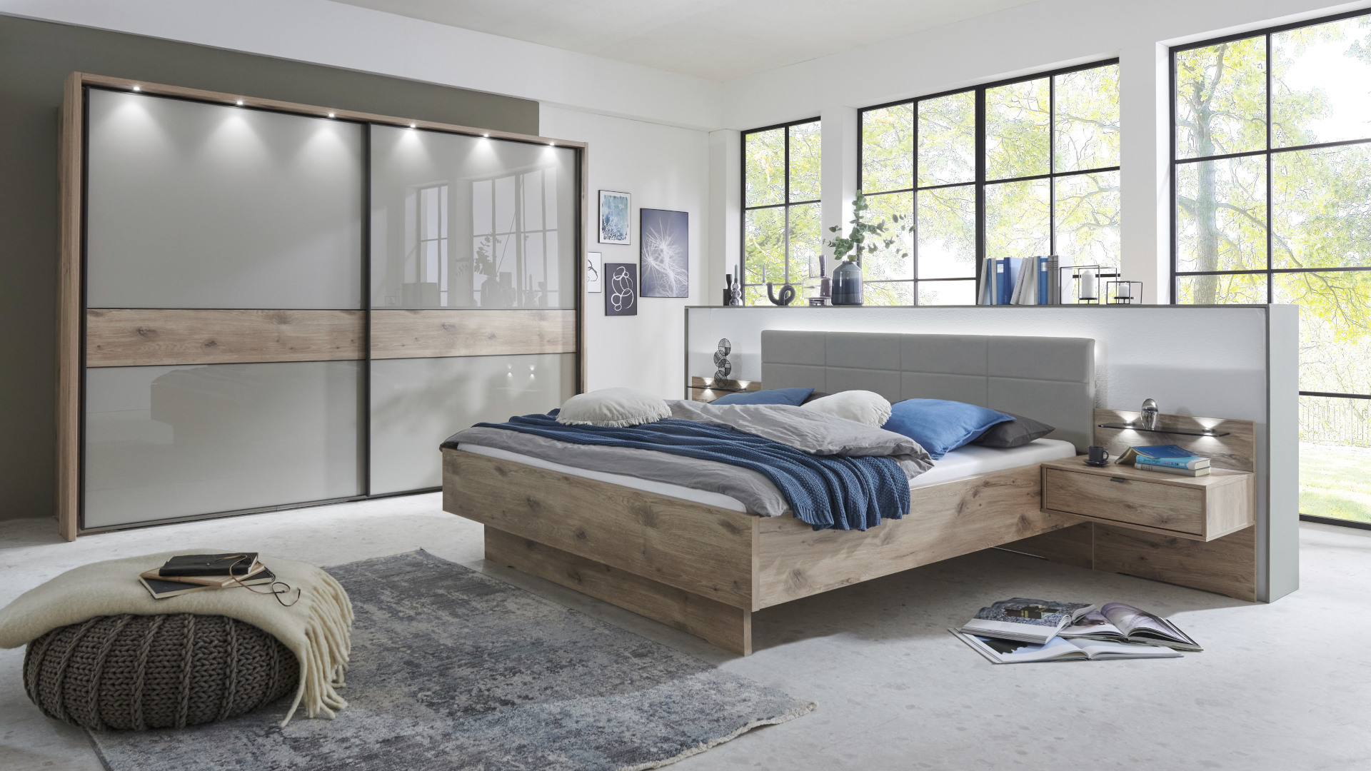 Die Schlafzimmerserie Treviso von Wiemann mit einem Bett mit Nachtkästen und einem Kleiderschrank mit kieselgrauer Glasfront.