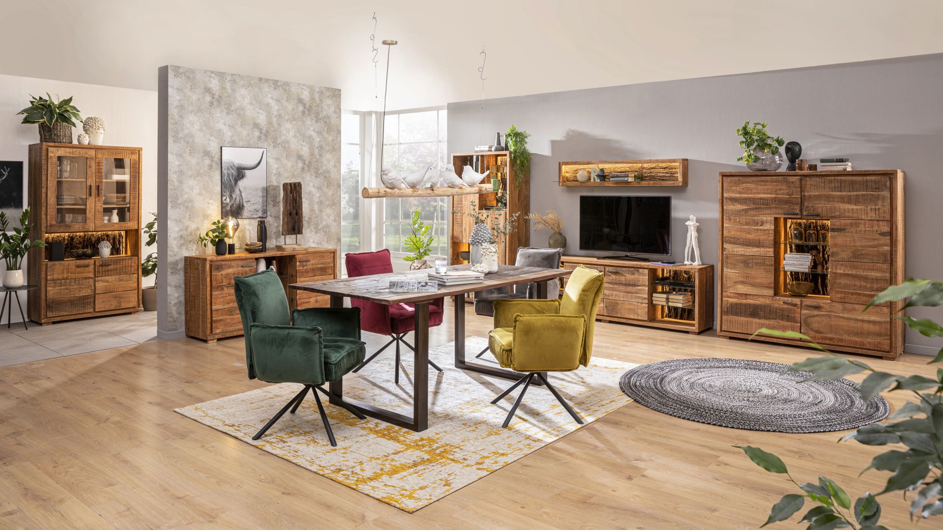 Ein Esszimmer mit Massivholzmöbeln der Marke Wolf Möbel, darunter der Esstisch Bark  in der Größe 180 x 90 cm aus recyceltem Altholz und Metall und das Highboard Bark 4067 aus Akazie und inklusive Beleuchtung.