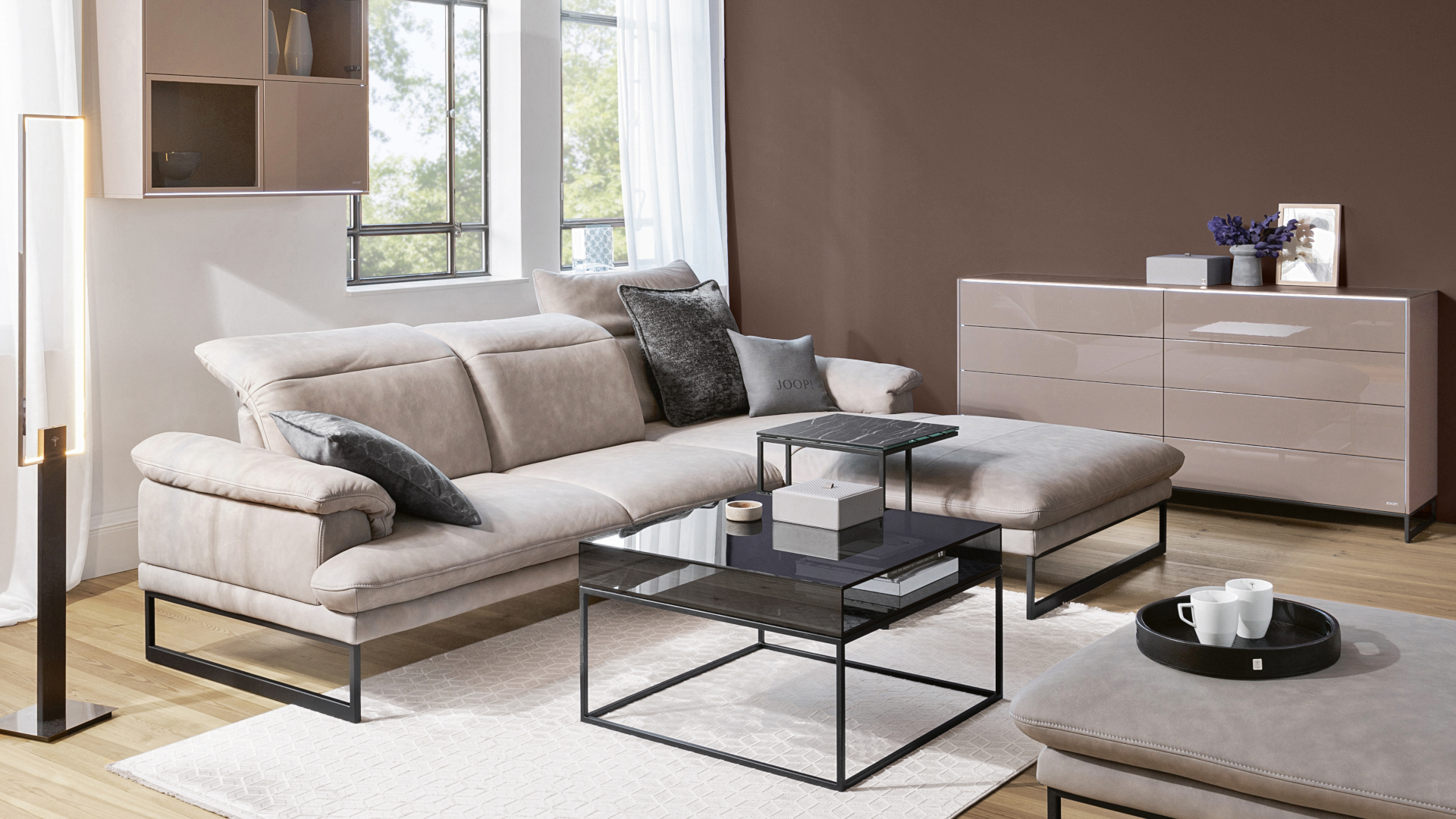 Das beige Leder-Ecksofa Studio der Marke JOOP! mit Hocker in einem Wohnzimmer mit Erdfarben