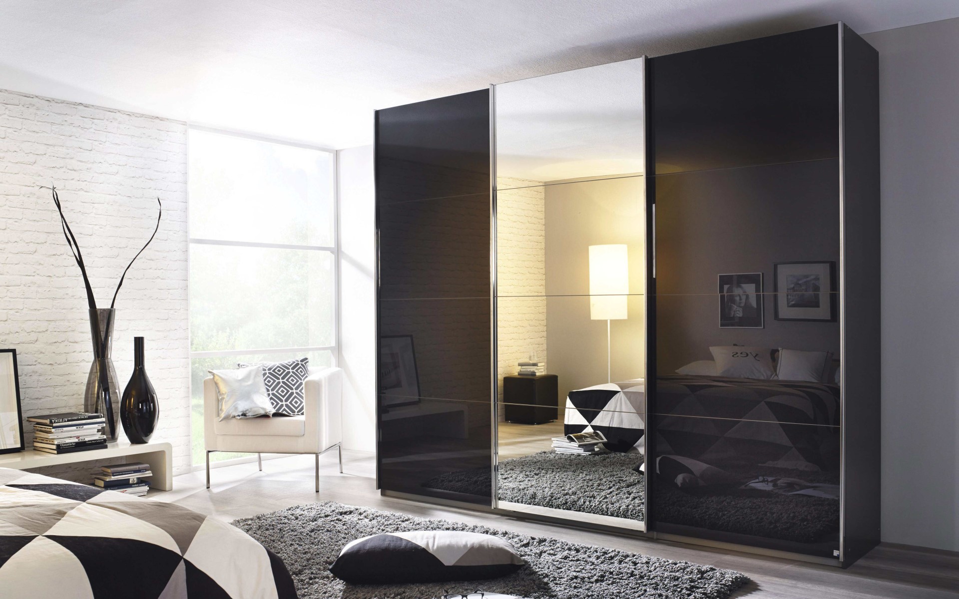 Schwebetürenschrank Kulmbach aus dem Hause rauch ORANGE mit einer Oberfläche aus schwarzem Glas in einem modernen, in schwarz-weiß gehaltenem Schlafzimmer