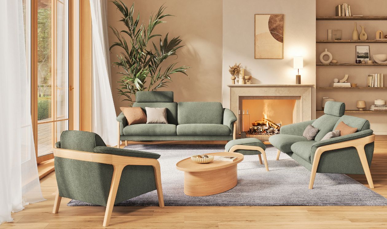 Eine Sitzgruppe aus Polstermöbeln der Transforma-Serie Nido der SEGMÜLLER Werkstätten mit hellen Holzgestellen und grünen Stoffbezügen steht in einem modernen Wohnzimmer mit Kamin.