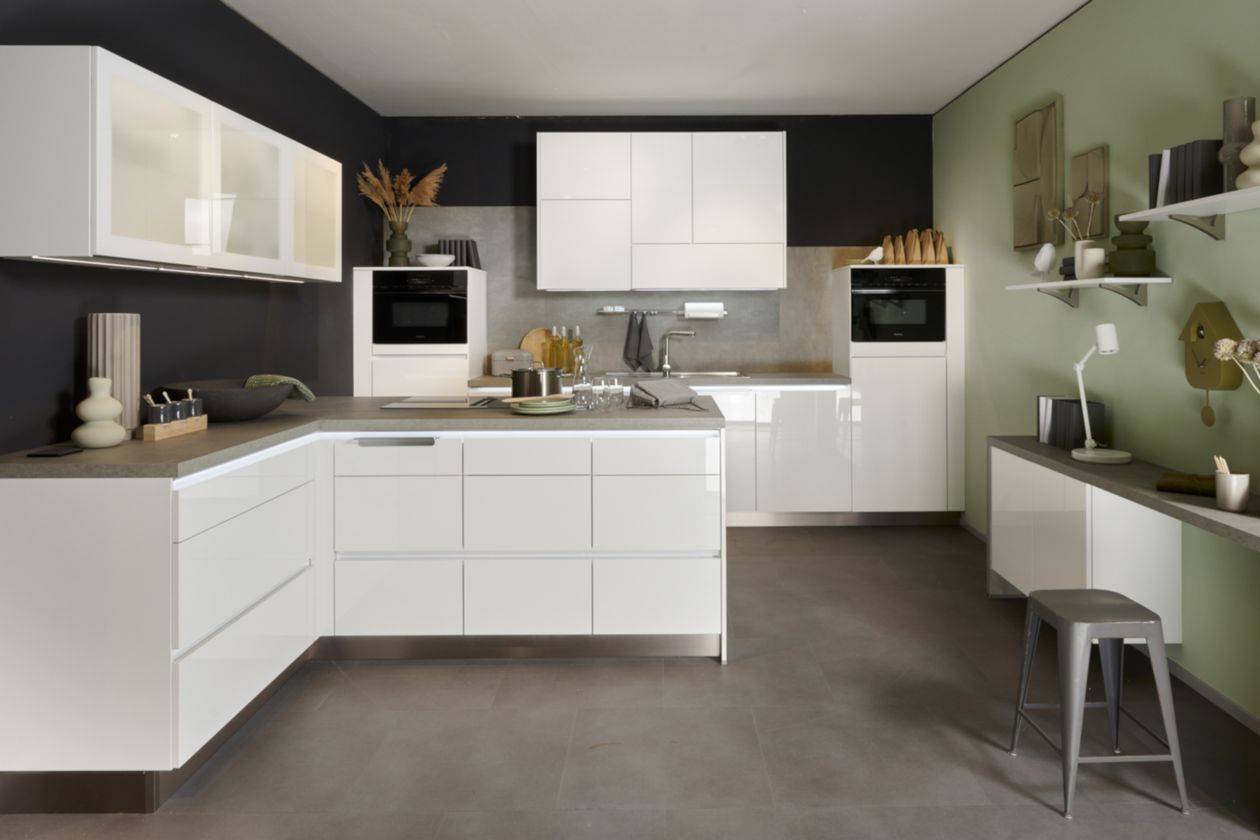 Moderne Küche mit weißen Schränken, einer zentralen Kochinsel und dunklen Arbeitsplatten. Elegante Geräte sind in das Design integriert. Akzentwand in Salbeigrün.