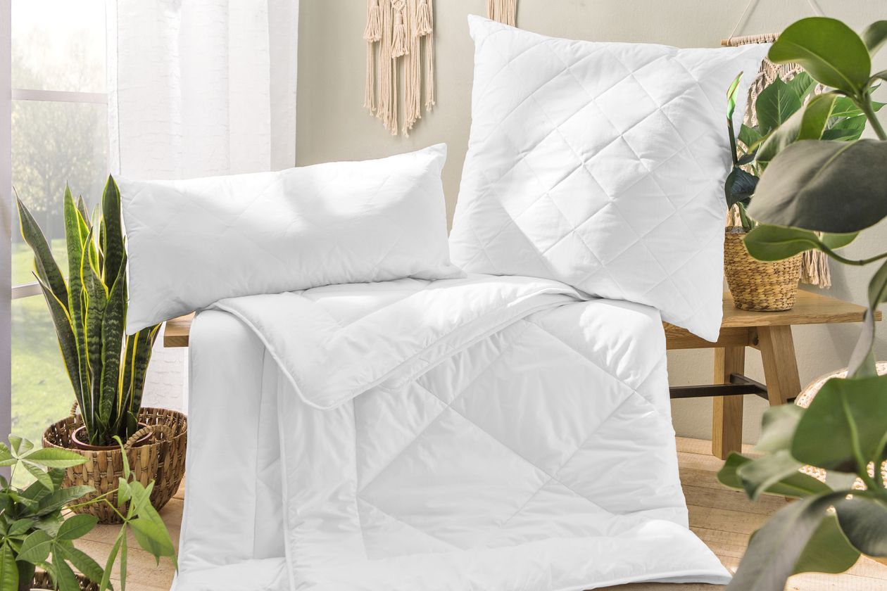 Die weiße Bettdecke und Kopfkissen der Serie Margarete von Fürstenhof aus Baumwolle auf eine Holzbank