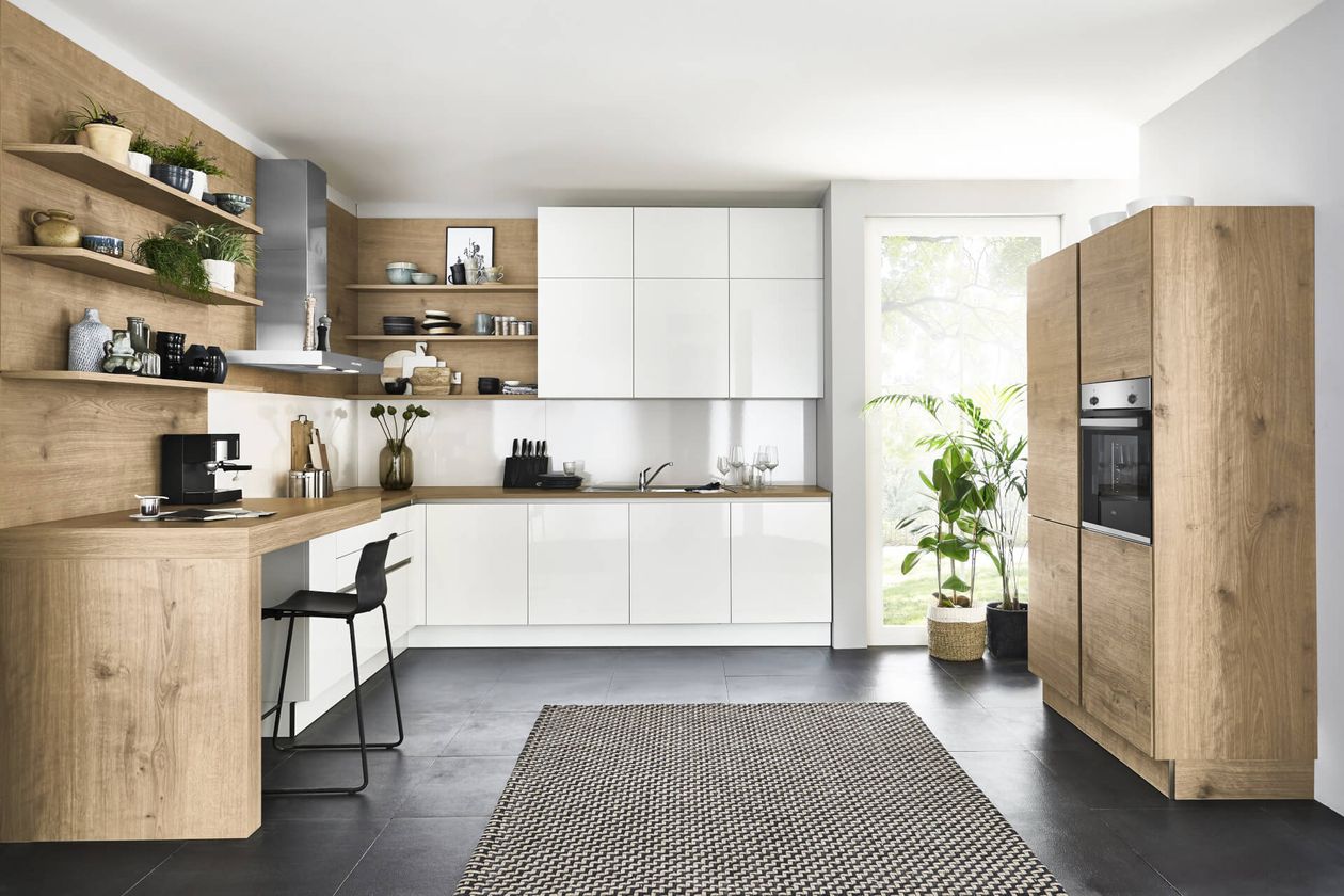 Küche mit Holzschränken, weißen Arbeitsplatten, Wandregalen, Einbaugeräten und einem schwarzen Stuhl. Topfpflanzen in der Nähe eines Fensters.