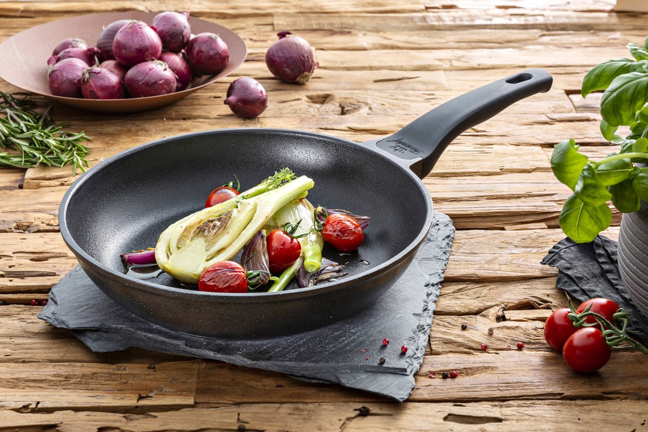 Die schwarze Aluminium-Pfanne Nizza Plus von Fürstenhof auf einer Schieferplatte. In ihr befindet sich gebratenes Gemüse.