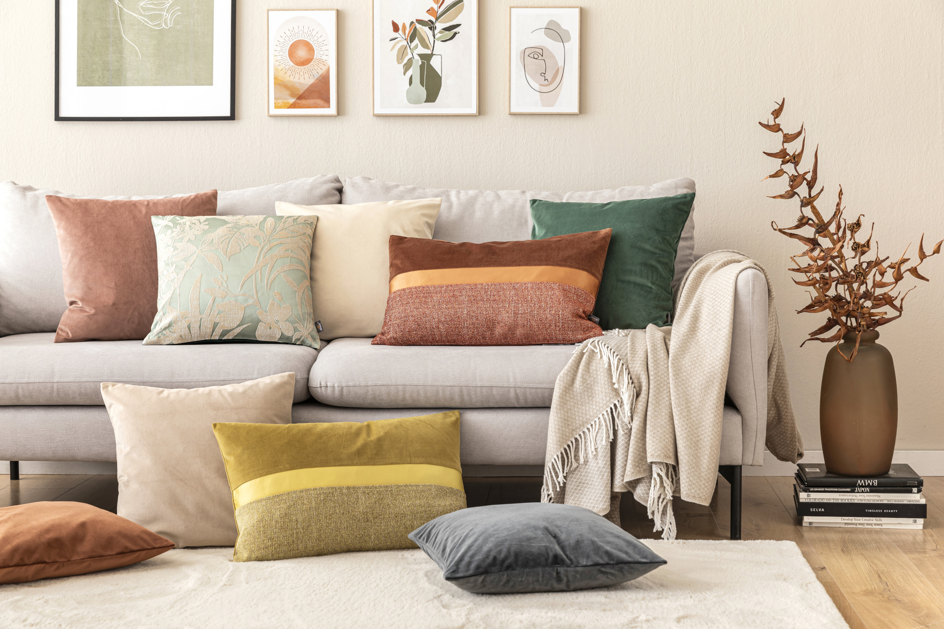 Ein Sofa, auf dem verschiedenen Wohntextilien der Marke Fürstenhof platziert sind, unter anderem der Plaid Amalia in Beige mit Fransen und die Kissenhülle Gracia Blumenranke aus recyceltem Samt in Salbeigrün.