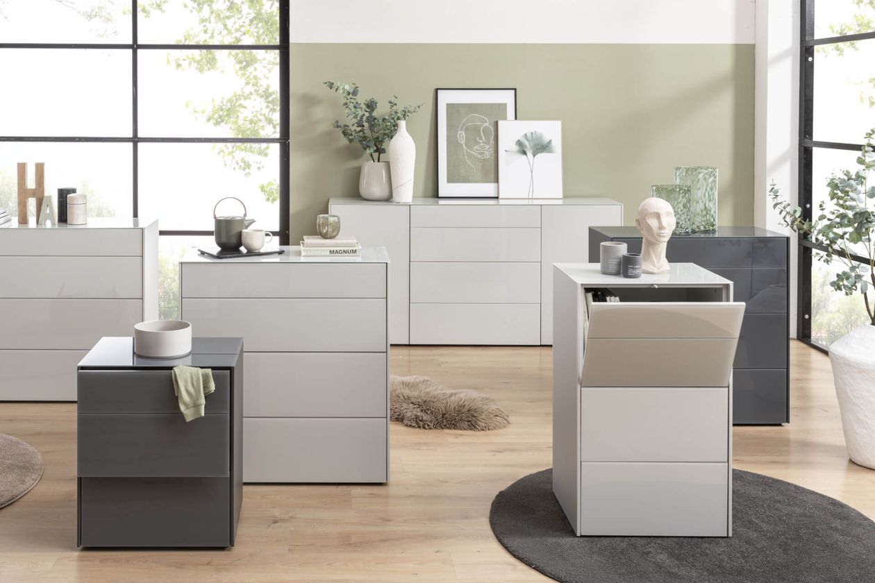 Sechs Kommoden in verschiedenen Grautönen. Dekoriert mit diversen Objekten.