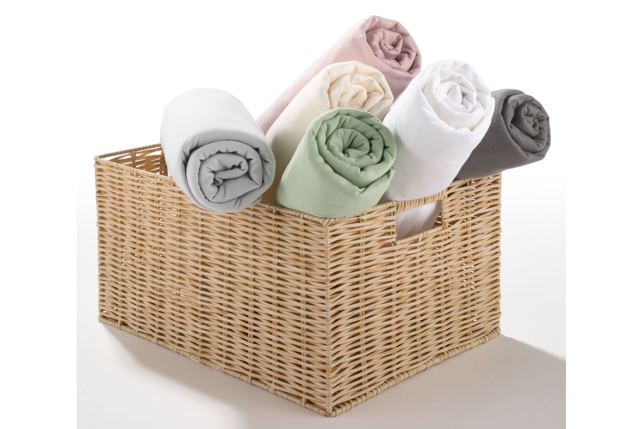 Sechs aufgerollte Spannbettlaken der Serie Sophie von Fürstenhof in einem Flechtkorb