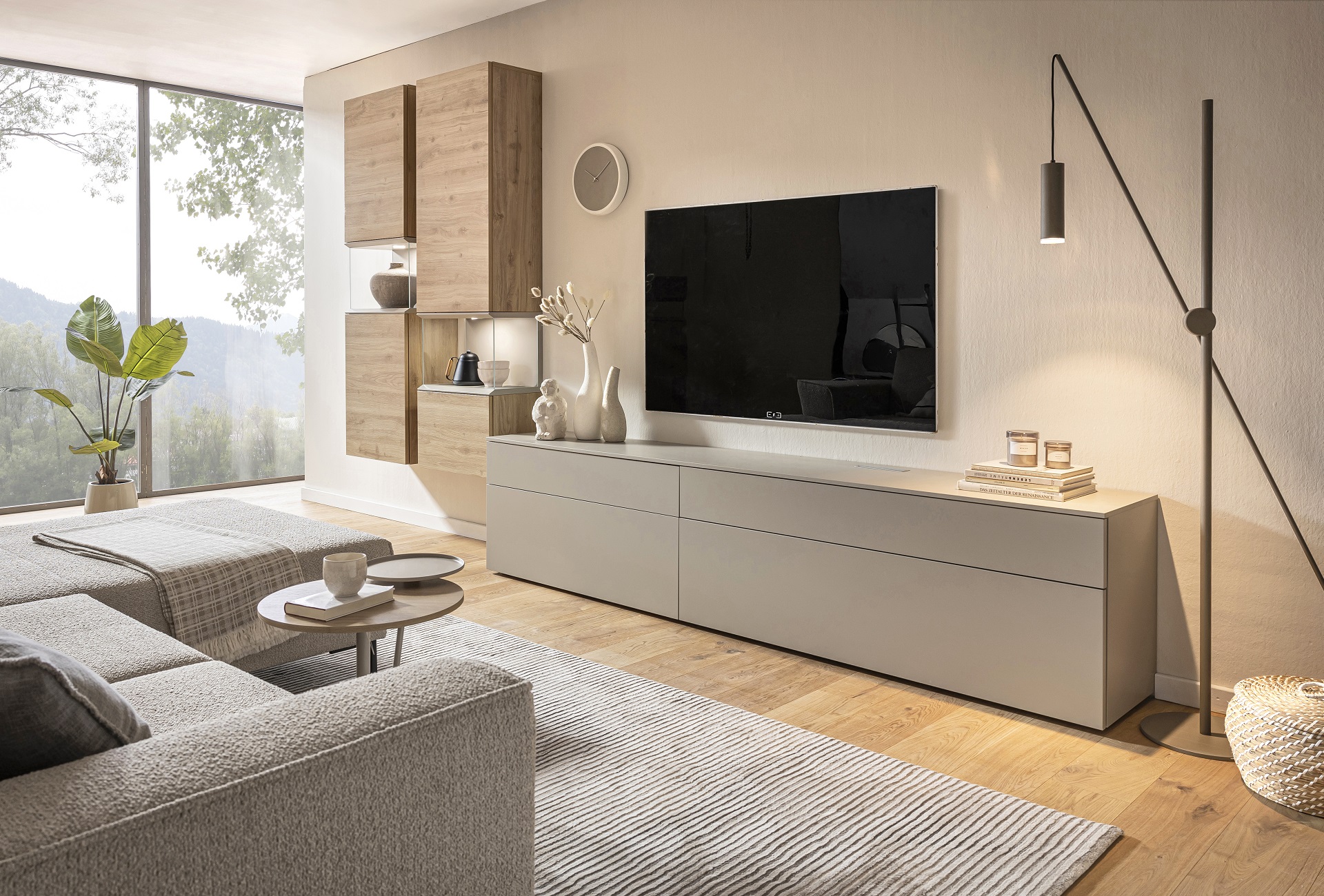 Modernes Wohnzimmer der Marke Sormani mit einer grifflosen Wohnwand in neutralen Farbtönen. Ein großes Fenster bietet einen Blick in die Natur.