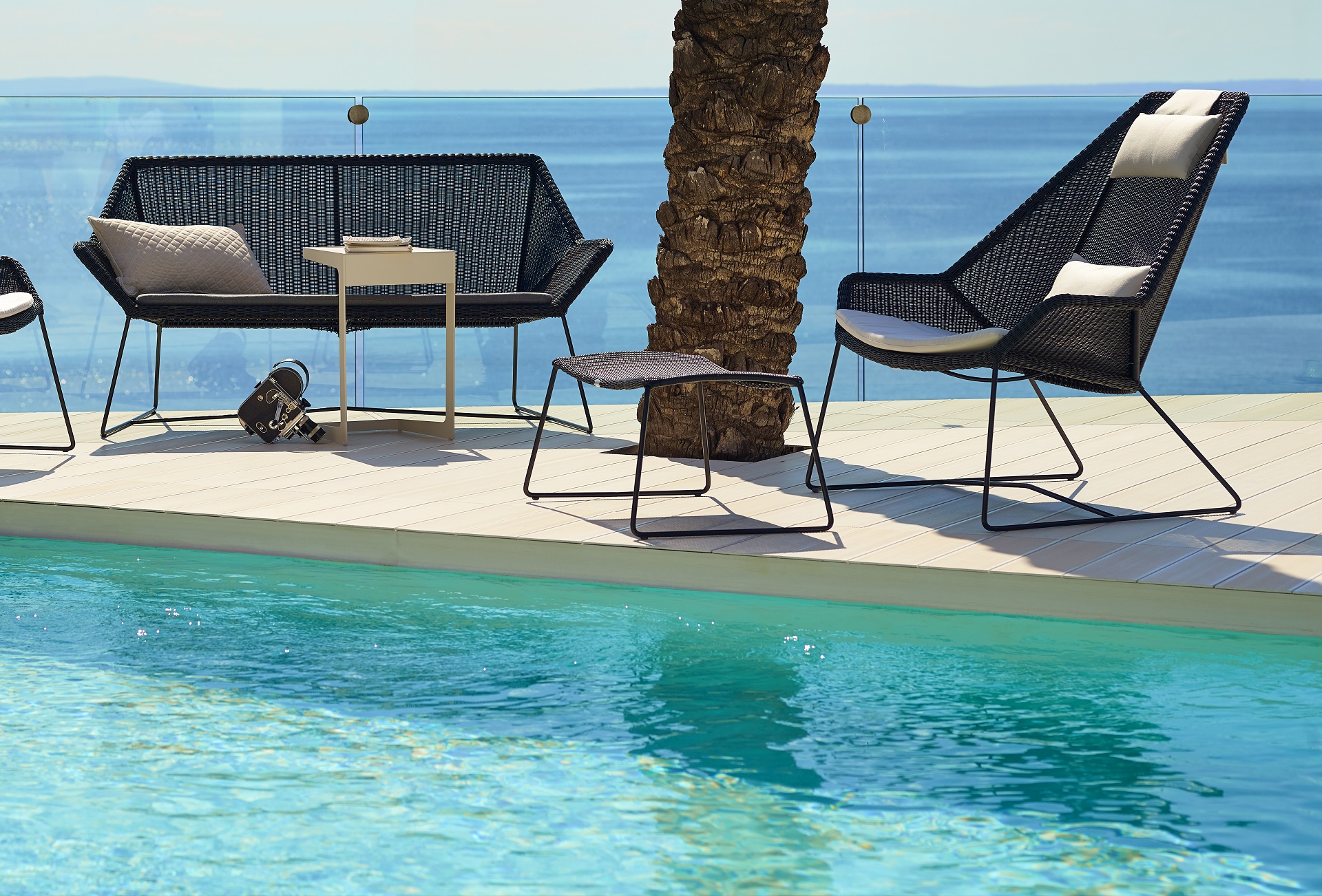 Gartenhocker Breeze von Cane Line aus Rattan & Geflecht mit Kufengestell vor einem Pool mit Blick auf das Meer