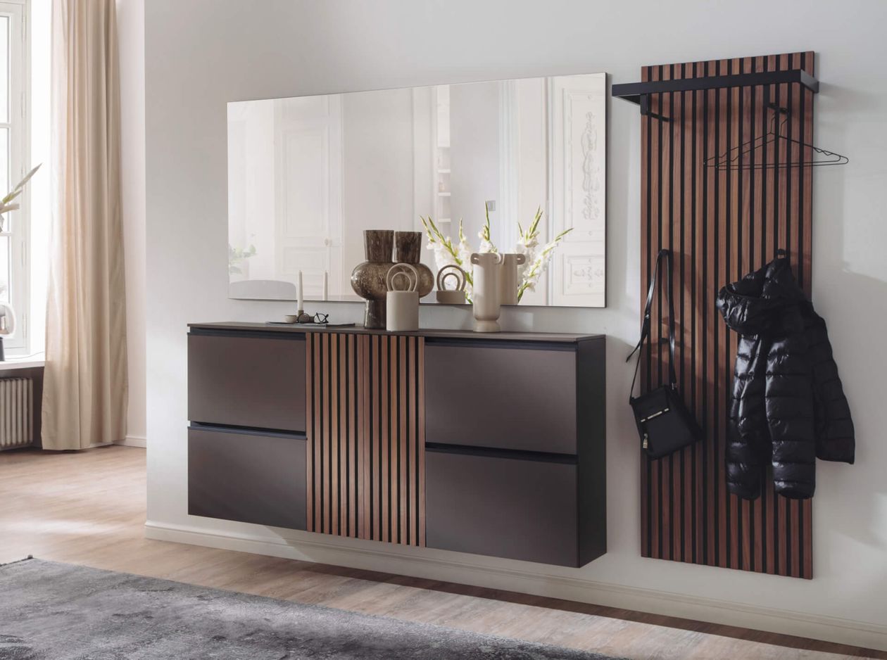 Ein moderner Flur mit einem eleganten Schrank, einem großen Spiegel, dekorativen Vasen und einer Garderobe, an der eine schwarze Jacke und eine Tasche an Holzlatten hängen.
