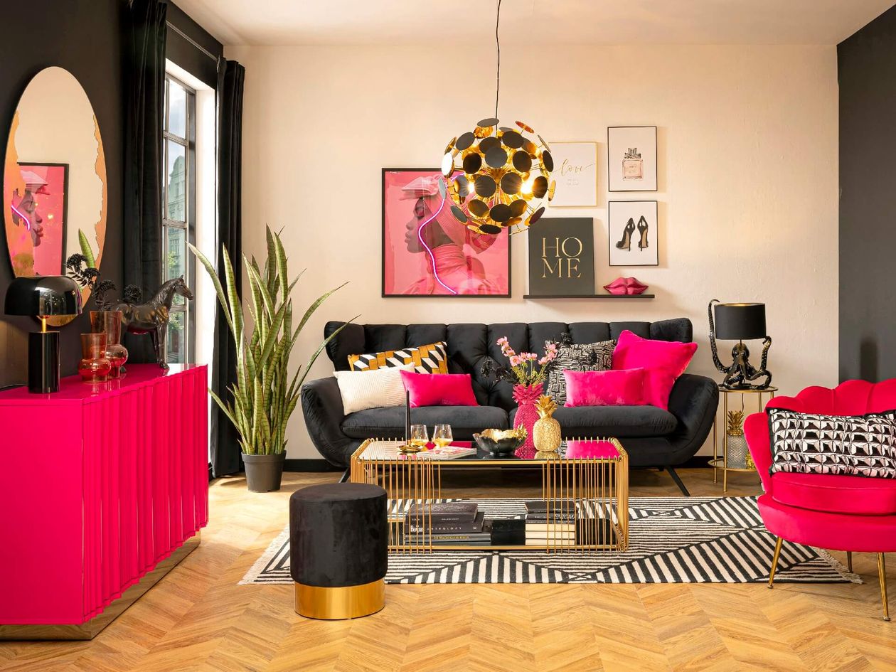 Modernes Wohnzimmer mit schwarzen und pinkfarbenen Akzenten, bestehend aus einem schwarzen Sofa, einem pinkfarbenen Sessel, einem geometrischen Teppich und einer goldenen Kugelpendelleuchte.