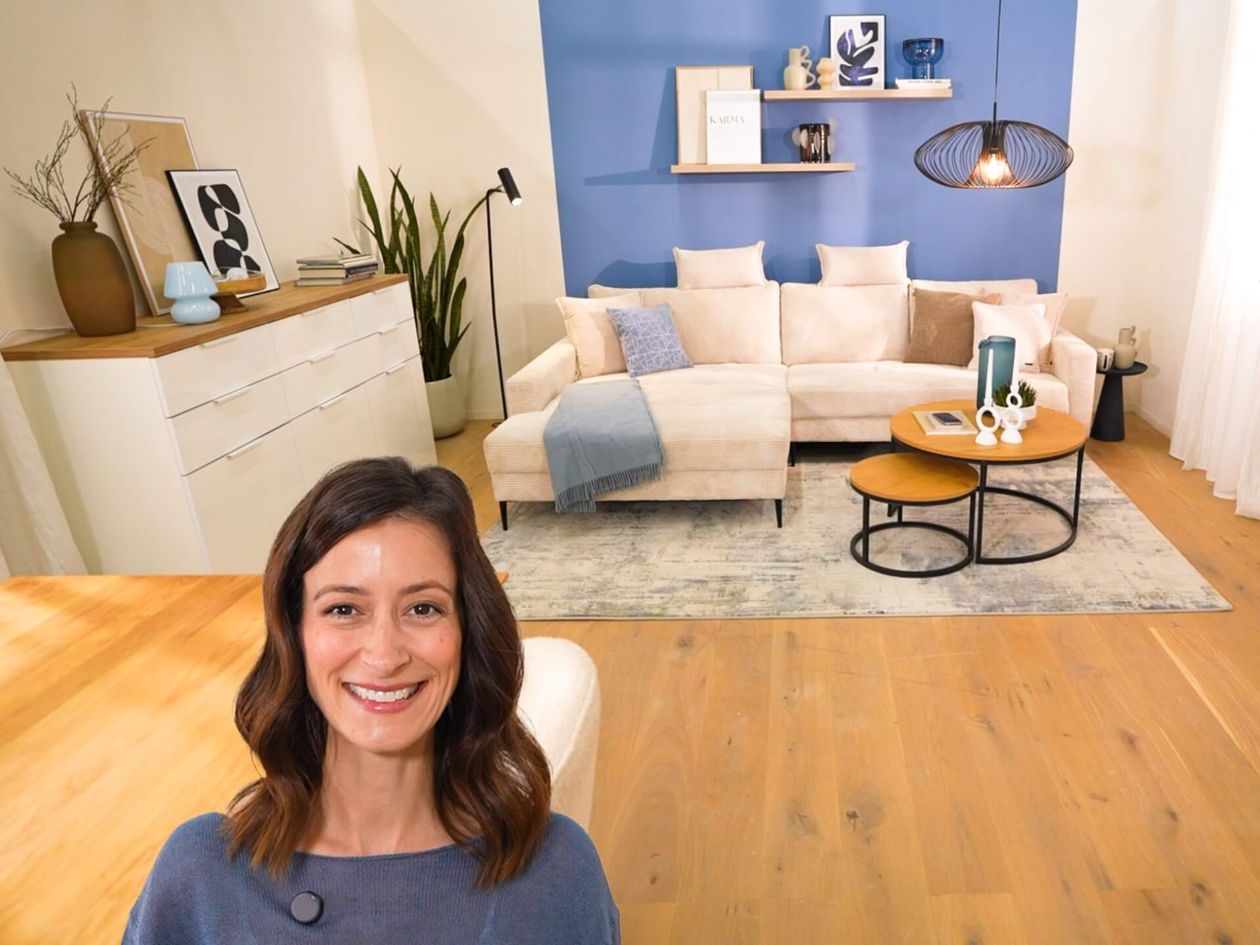 Lächelnde Frau in einem gemütlichen Wohnzimmer mit einem beigen Sofa, blauer Akzentwand, modernem Dekor und Holzboden.