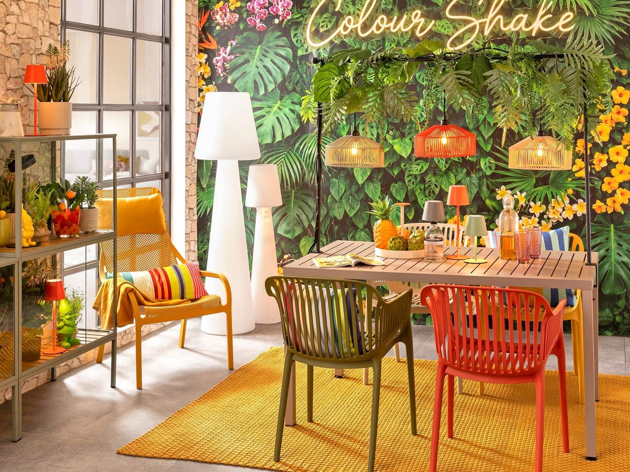 Lebhafte Terrasse im tropischen Stil mit farbenfrohen Stühlen, Holztisch, tropischen Pflanzen und leuchtender Dekoration unter Neonreklame.