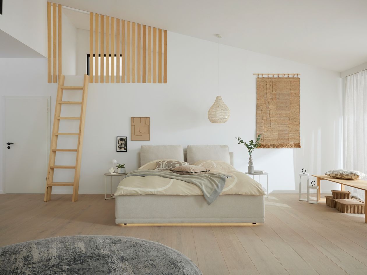 Helles gepolstertes Doppelbett in Beige mit hohem Kopfteil in einem minimalistischen Schlafzimmer mit Holzleiter, Flechtlampe und Wandteppich.